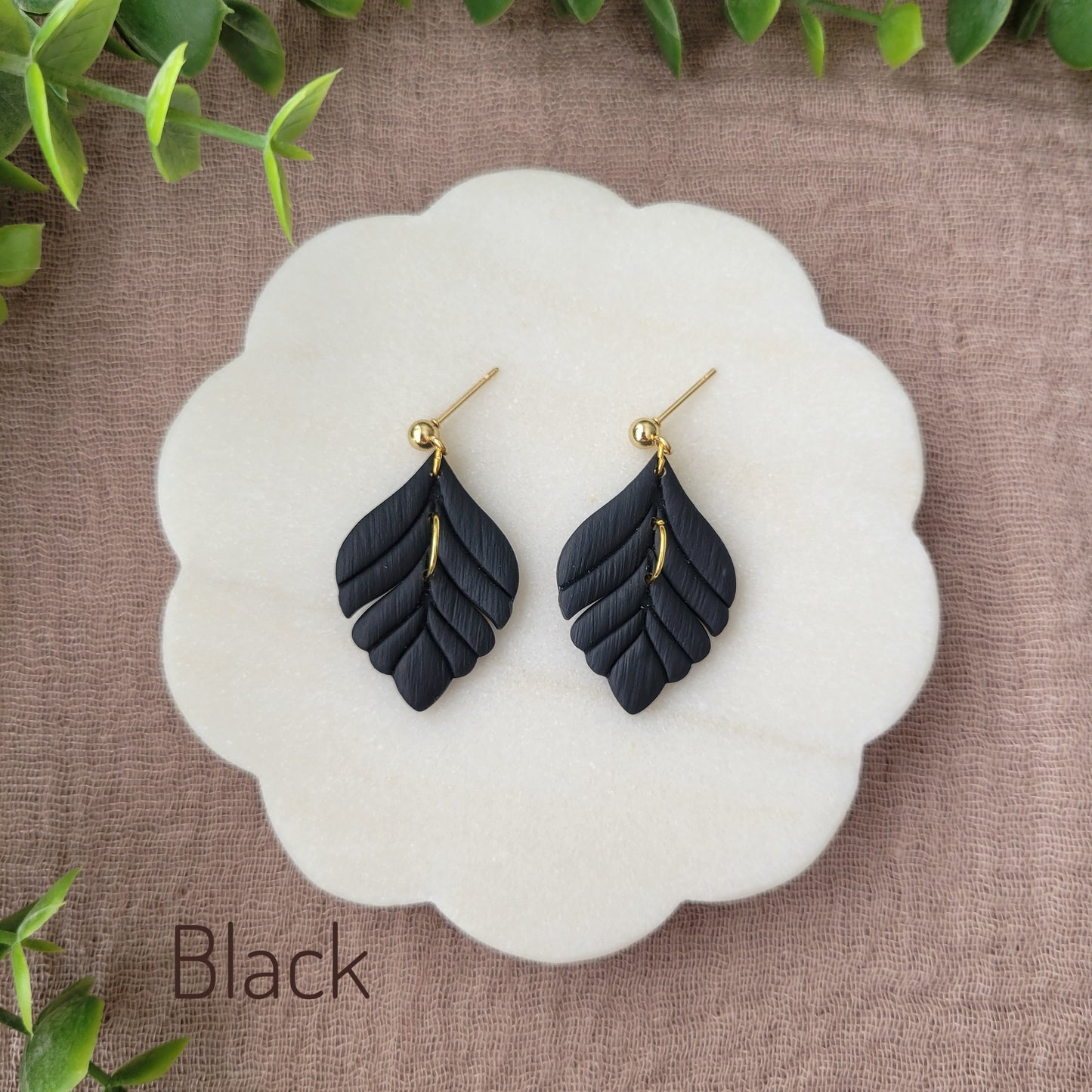 Top view of a pair of black elegant leaf shaped earrings displayed on a white round scalloped tray.