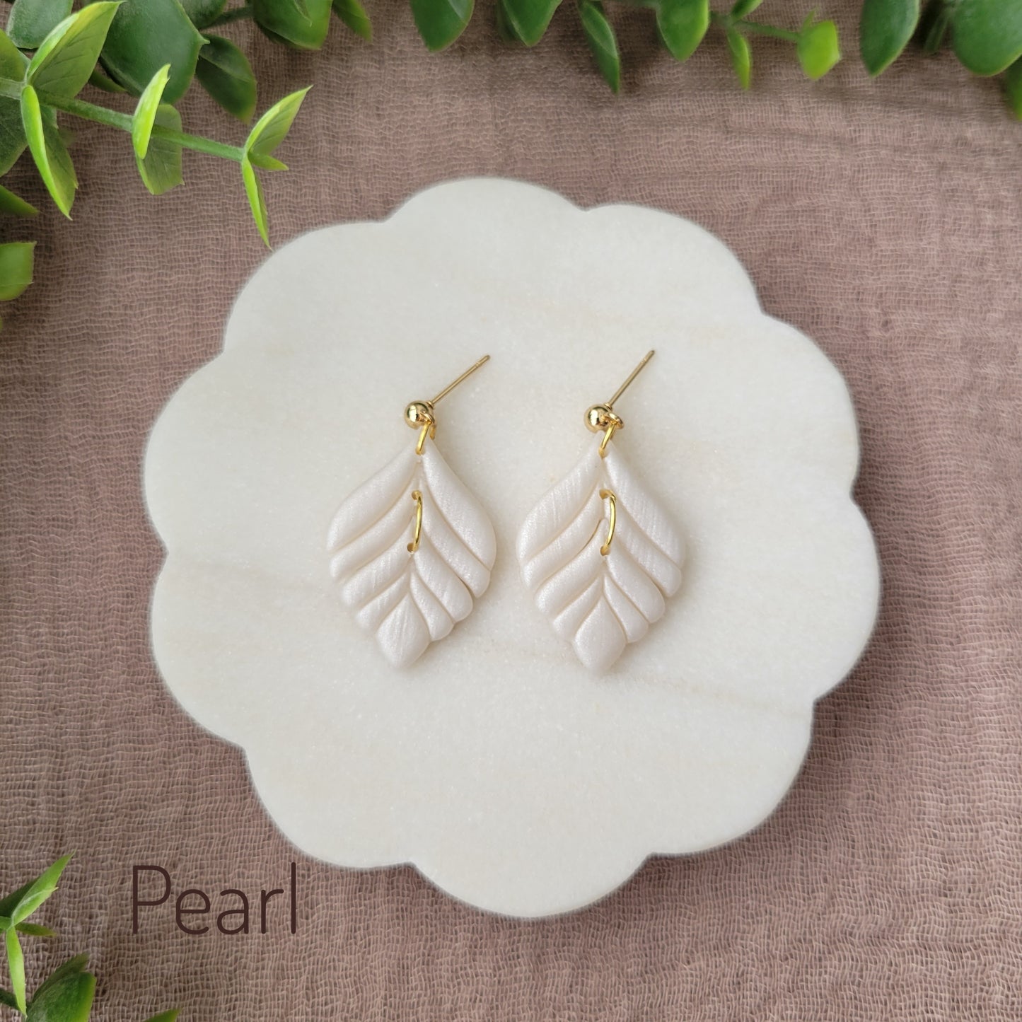 Top view of a pair of pearl elegant leaf shaped earrings displayed on a white round scalloped tray.