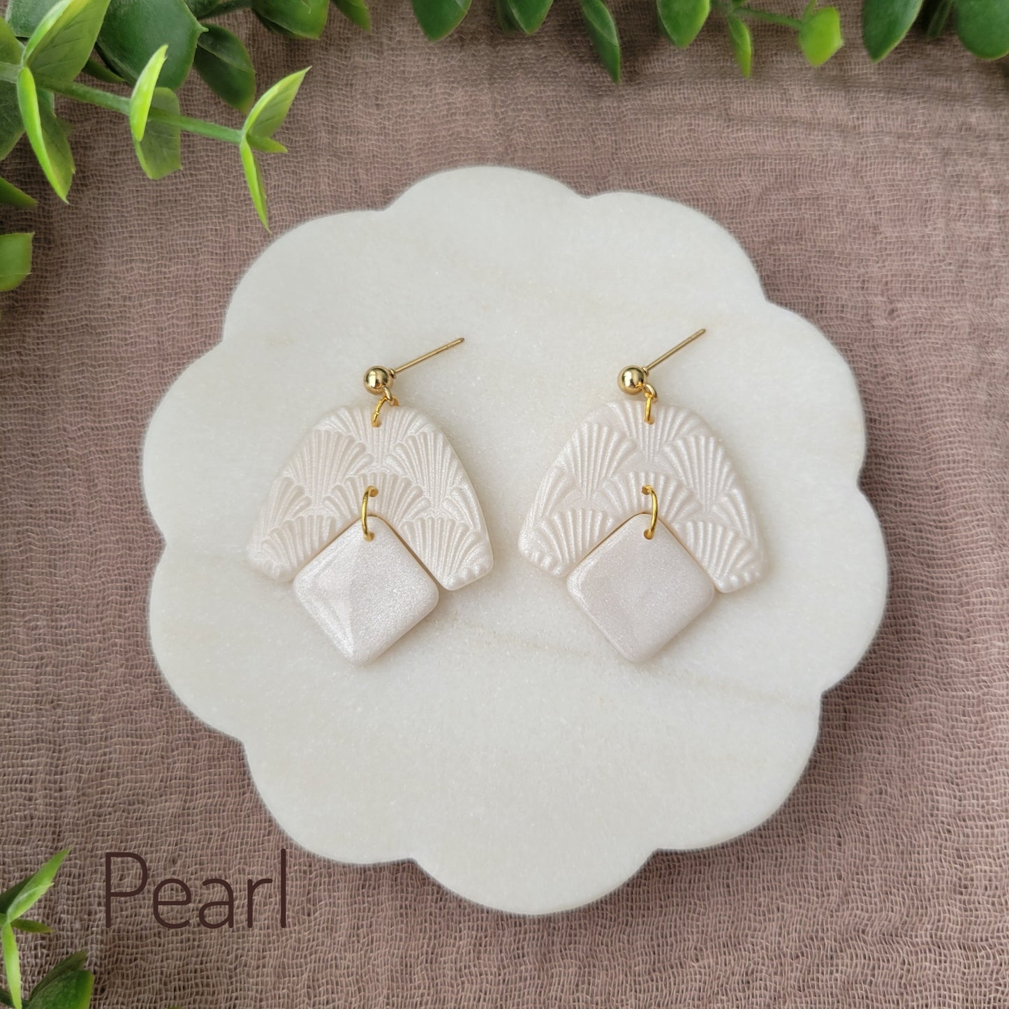 Top view of a pair of pearl colored earrings with a scalloped texture displayed on a white scalloped tray.