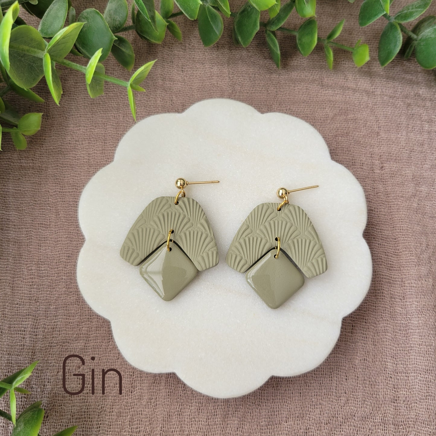 Top view of a pair of light green colored earrings with a scalloped texture displayed on a white scalloped tray.