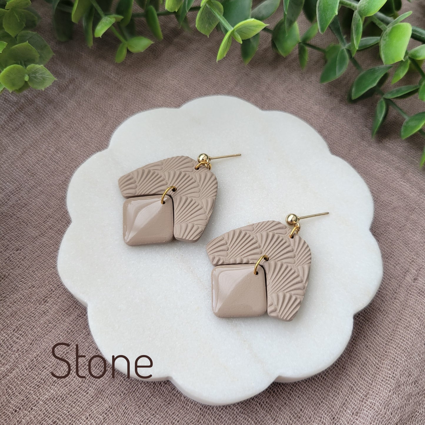 Side view of a pair of light brown colored earrings with a scalloped texture displayed on a white scalloped tray.