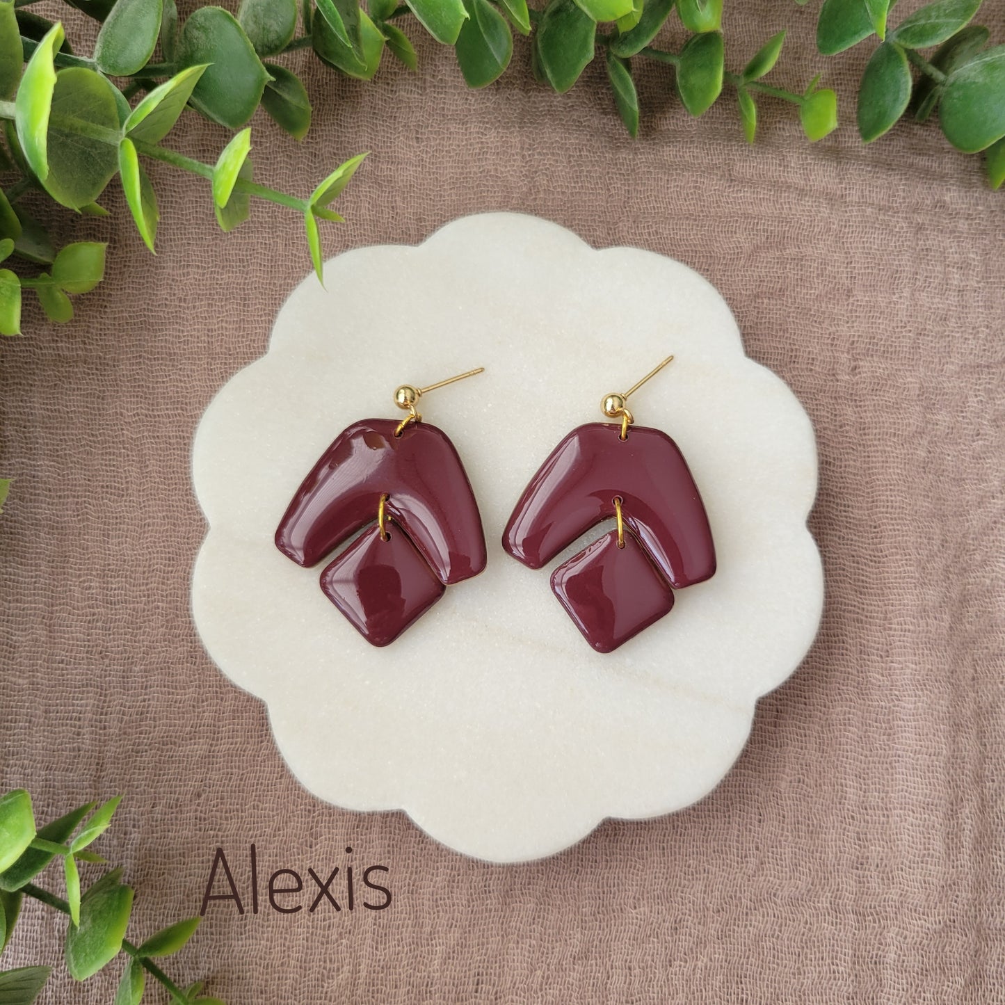 Top view of a pair of reddish purple earrings with shinny resin displayed on a white round scalloped tray.