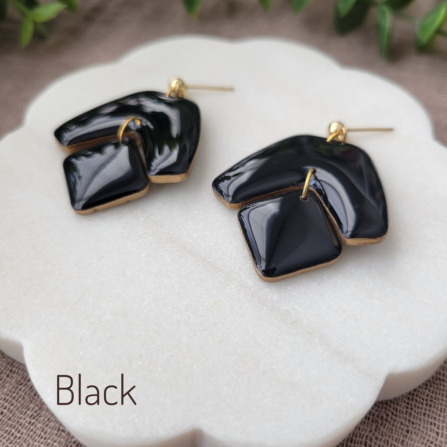 Side view of a pair of black earrings with shinny resin displayed on a white round scalloped tray.