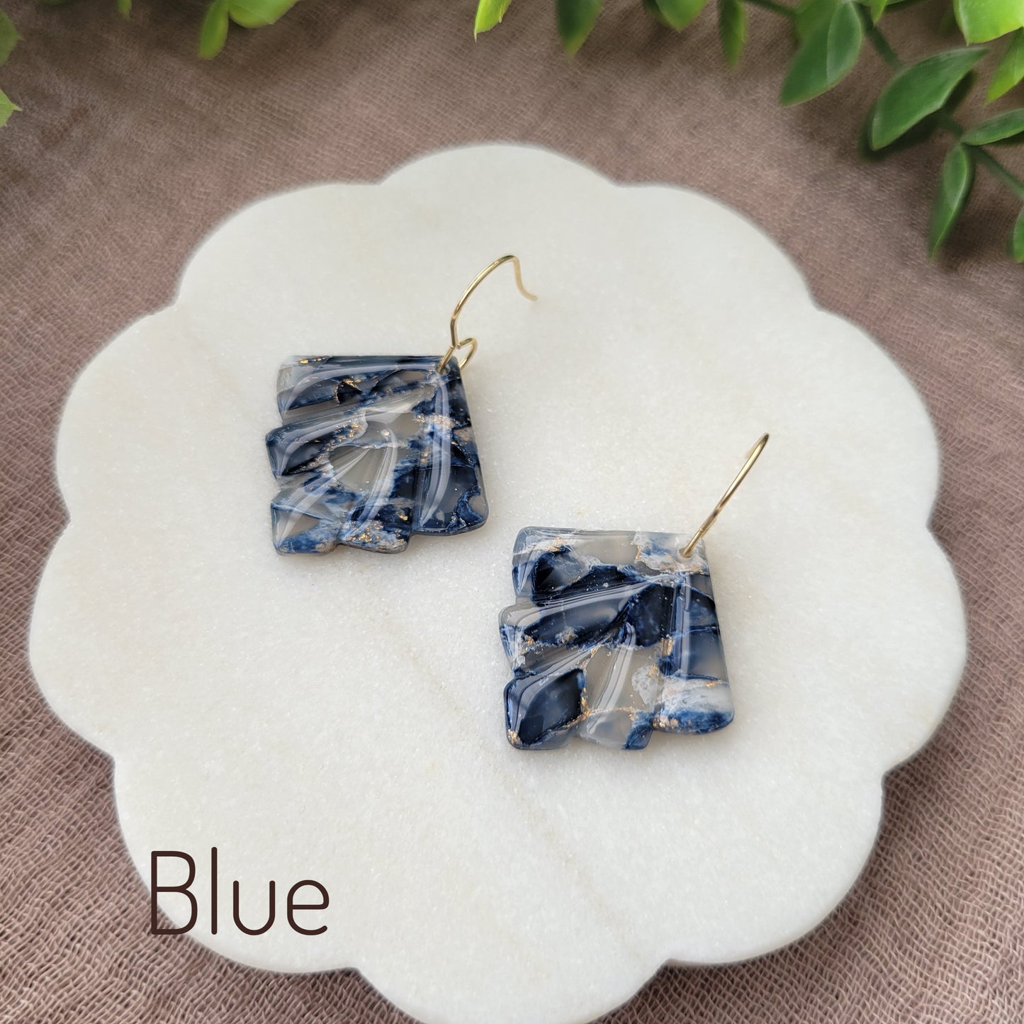 Side view of a pair of blue marbled earrings displayed on a white round scalloped tray.