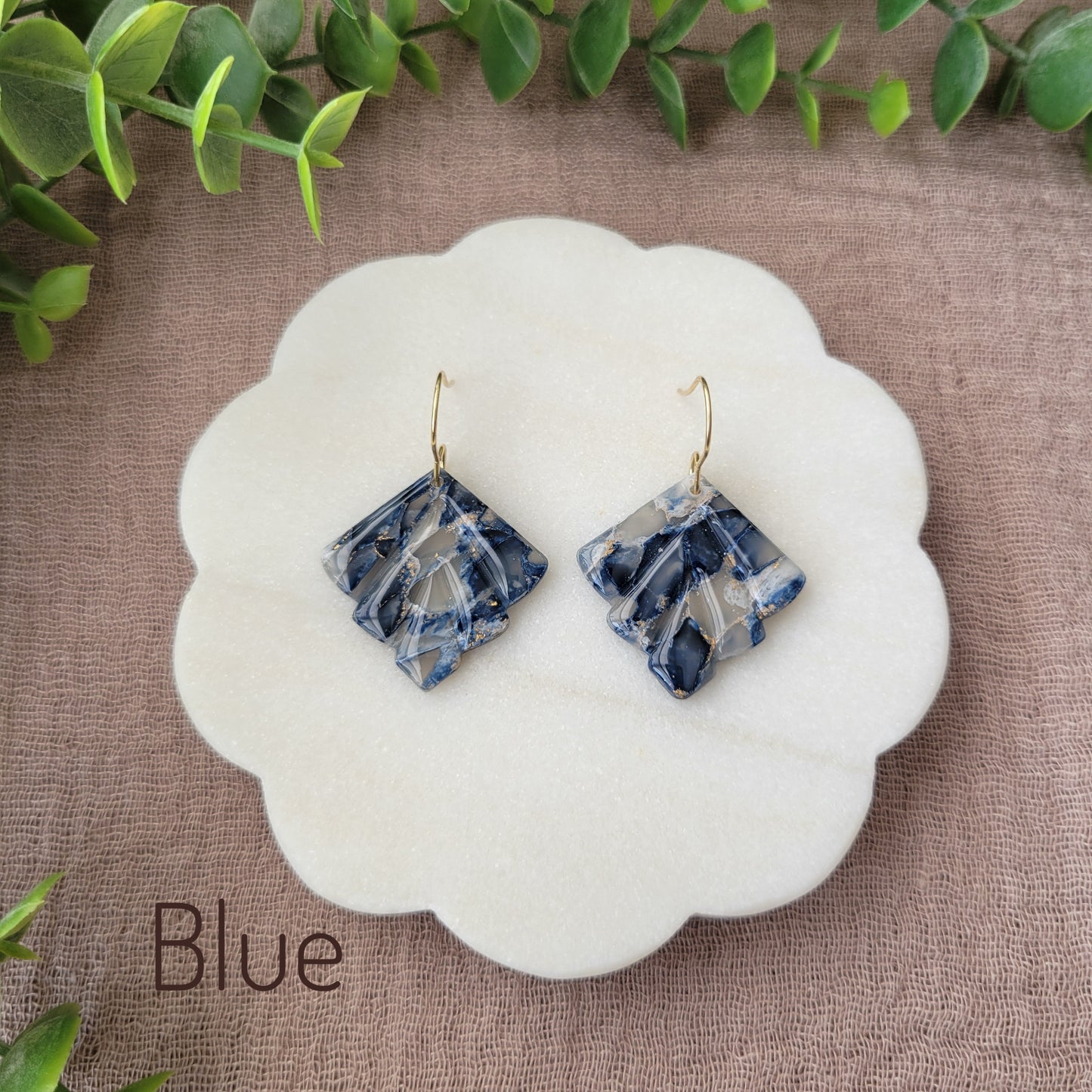 Top view of a pair of blue marbled earrings displayed on a white round scalloped tray.