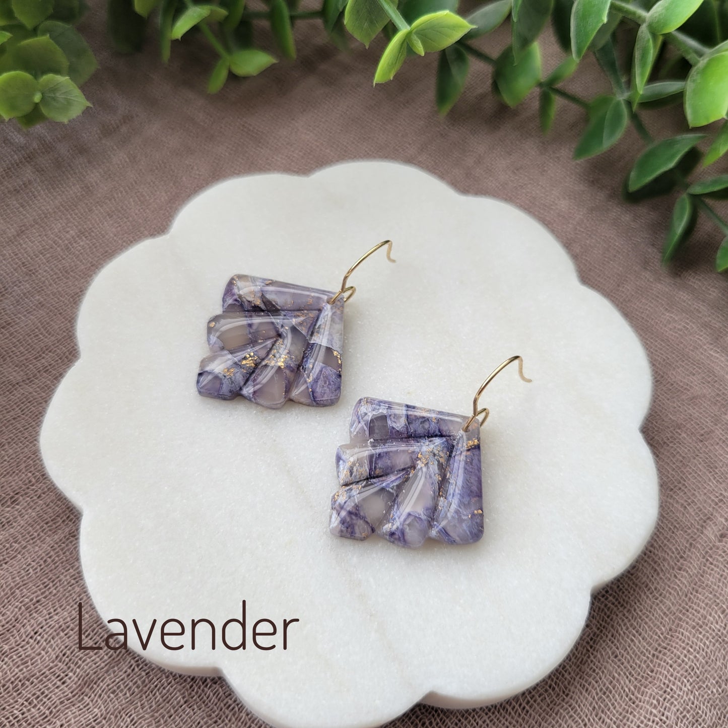 Side view of a pair of lavender marbled earrings displayed on a white round scalloped tray.