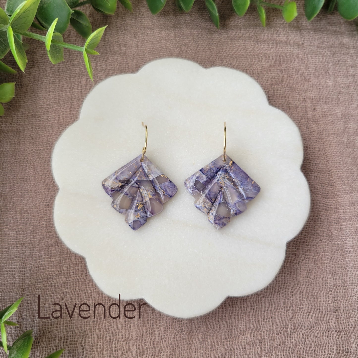 Top view of a pair of lavender marbled earrings displayed on a white round scalloped tray.