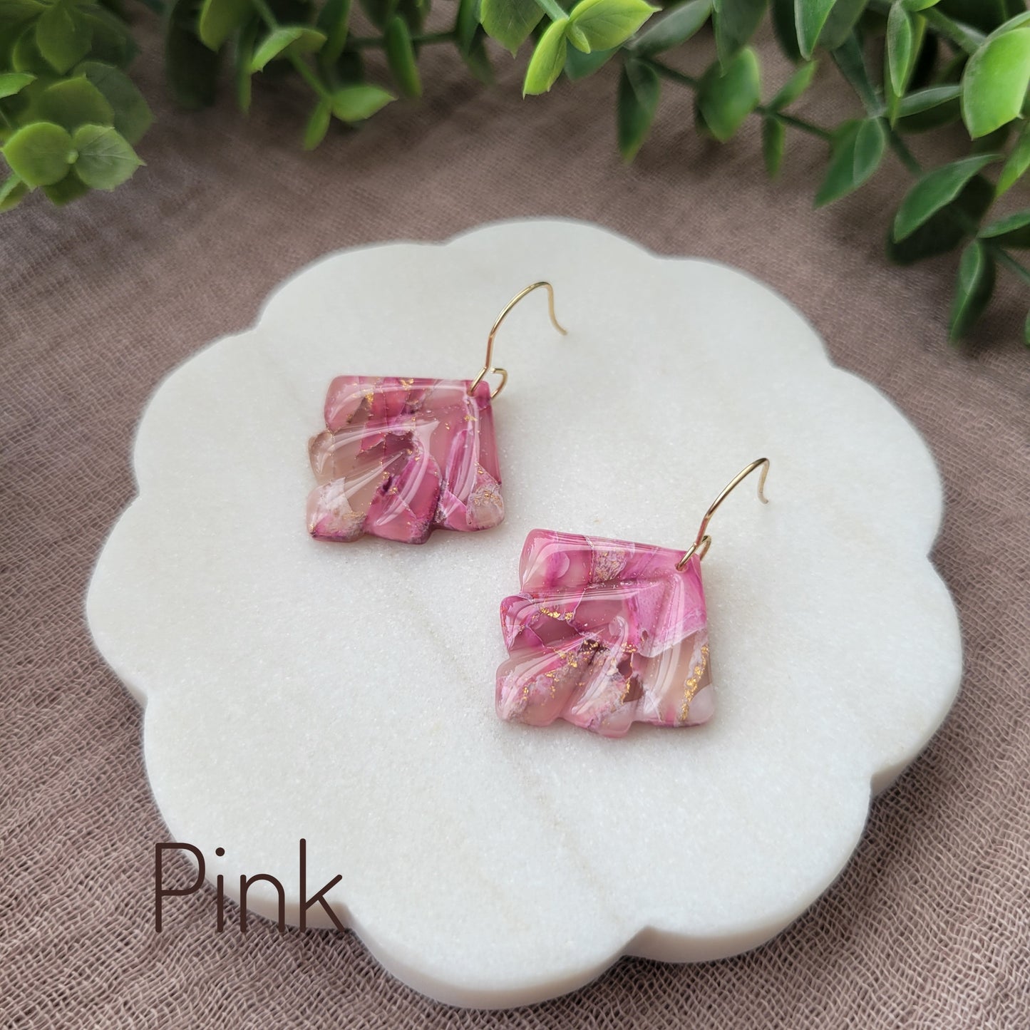 Side view of a pair of pink marbled earrings displayed on a white round scalloped tray.