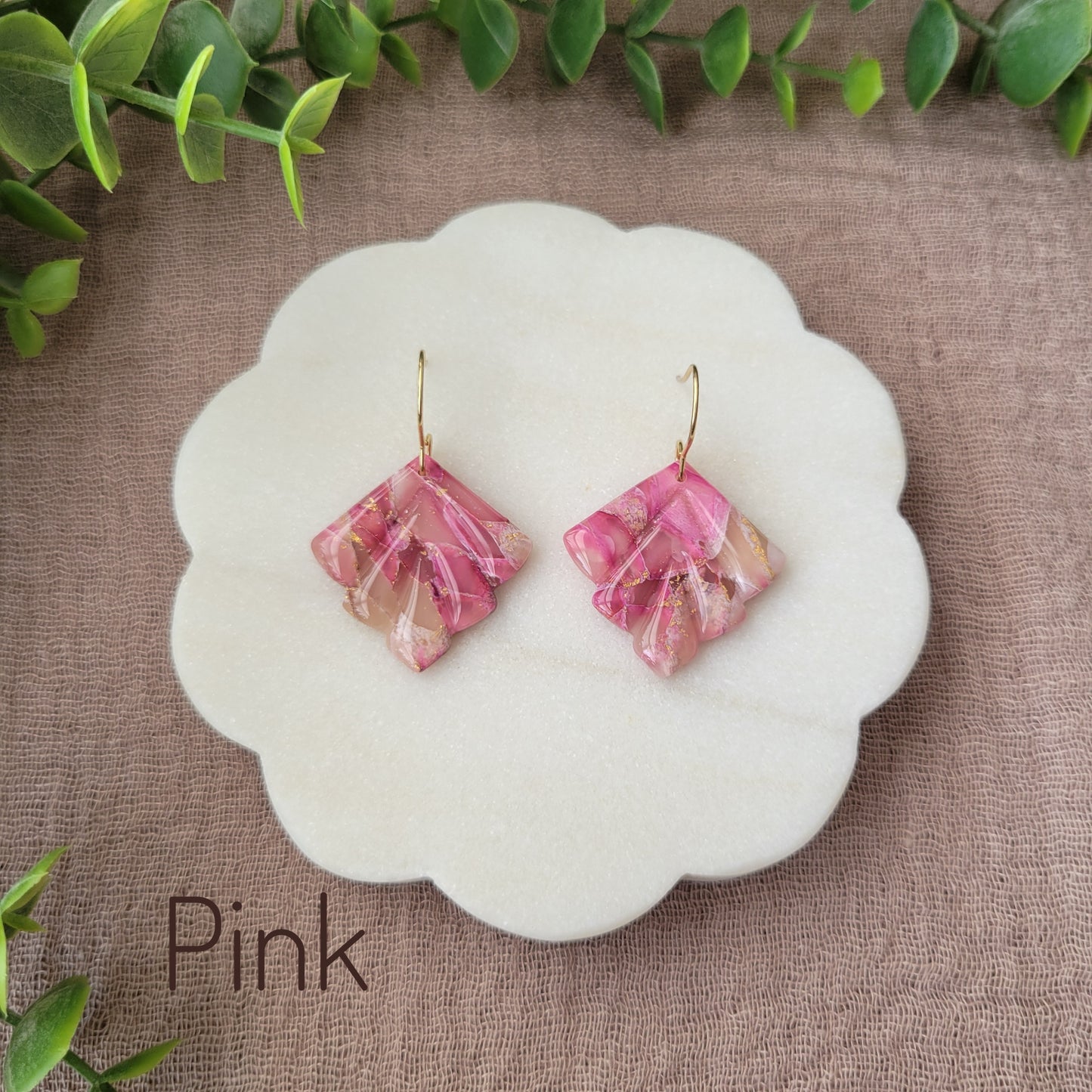 Top view of a pair of pink marbled earrings displayed on a white round scalloped tray.