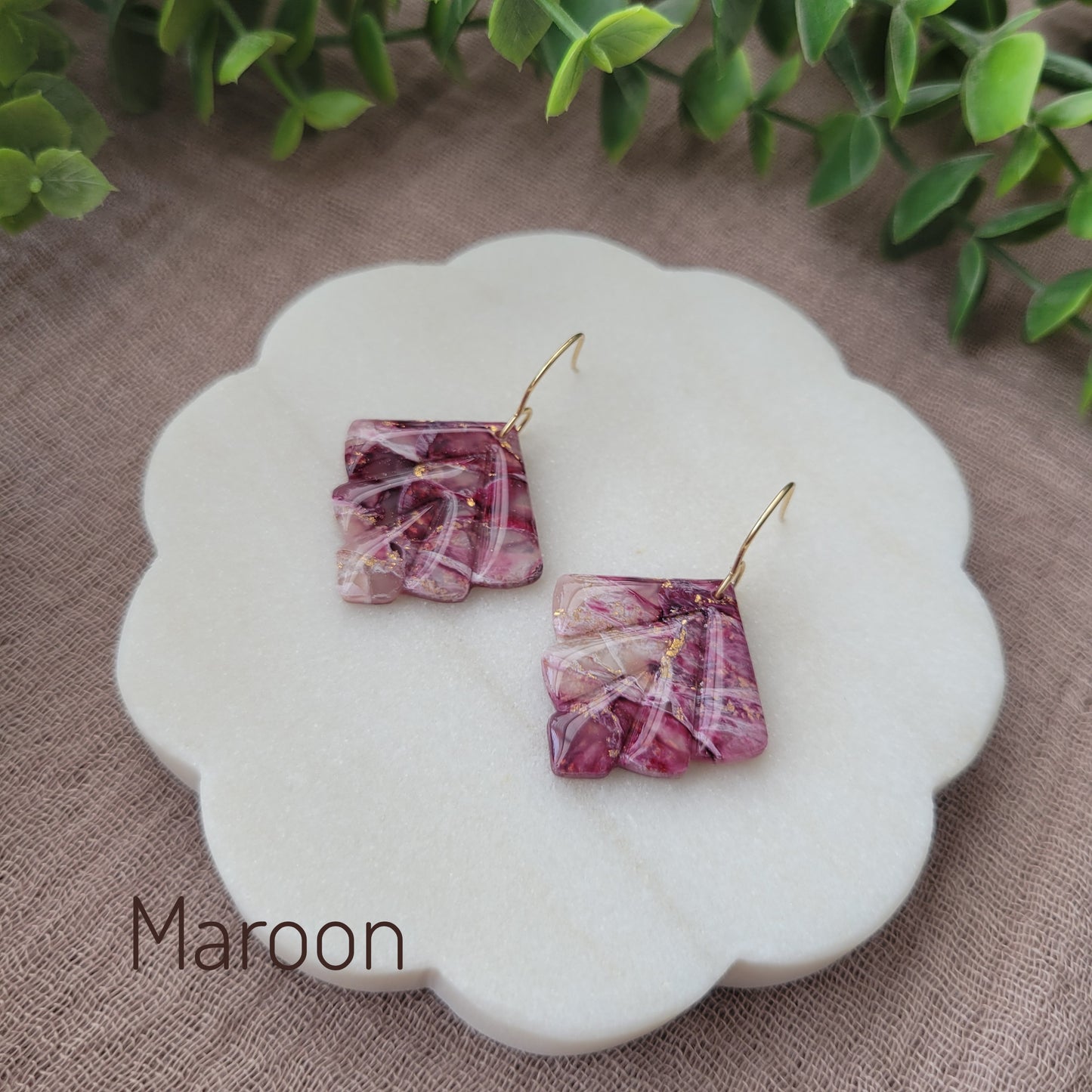 Side view of a pair of maroon marbled earrings displayed on a white round scalloped tray.