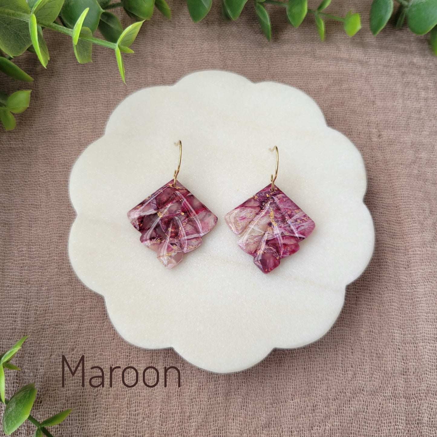 Top view of a pair of maroon marbled earrings displayed on a white round scalloped tray.