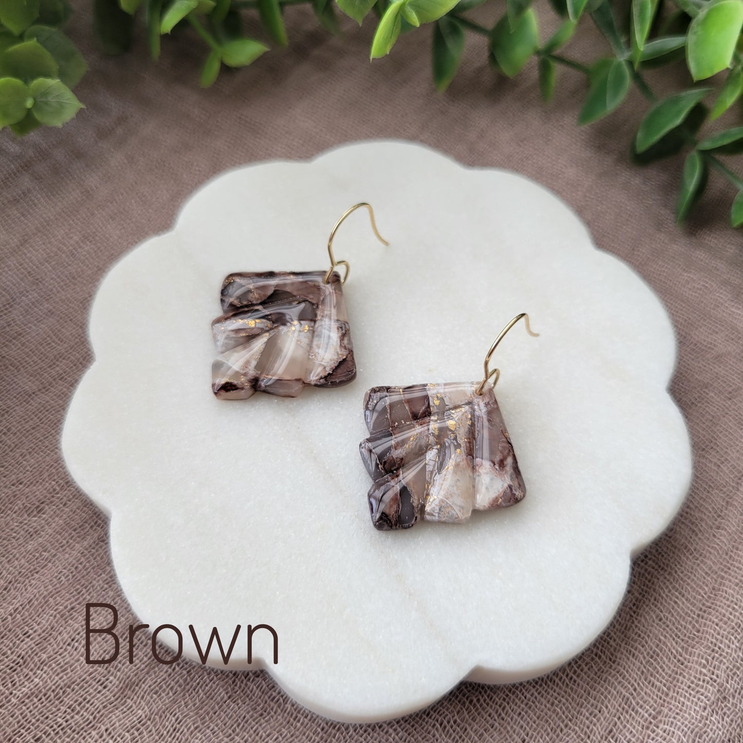 Side view of a pair of brown marbled earrings displayed on a white round scalloped tray.