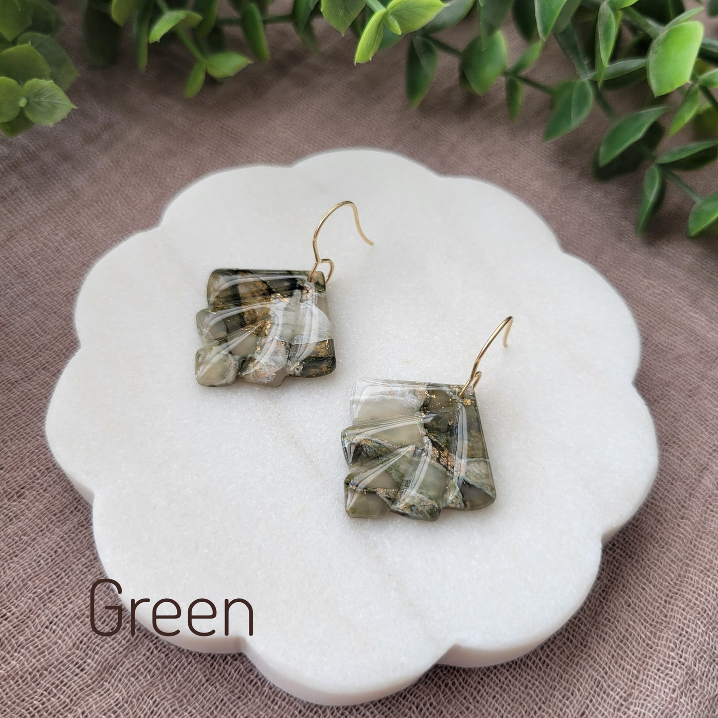 Side view of a pair of green marbled earrings displayed on a white round scalloped tray.
