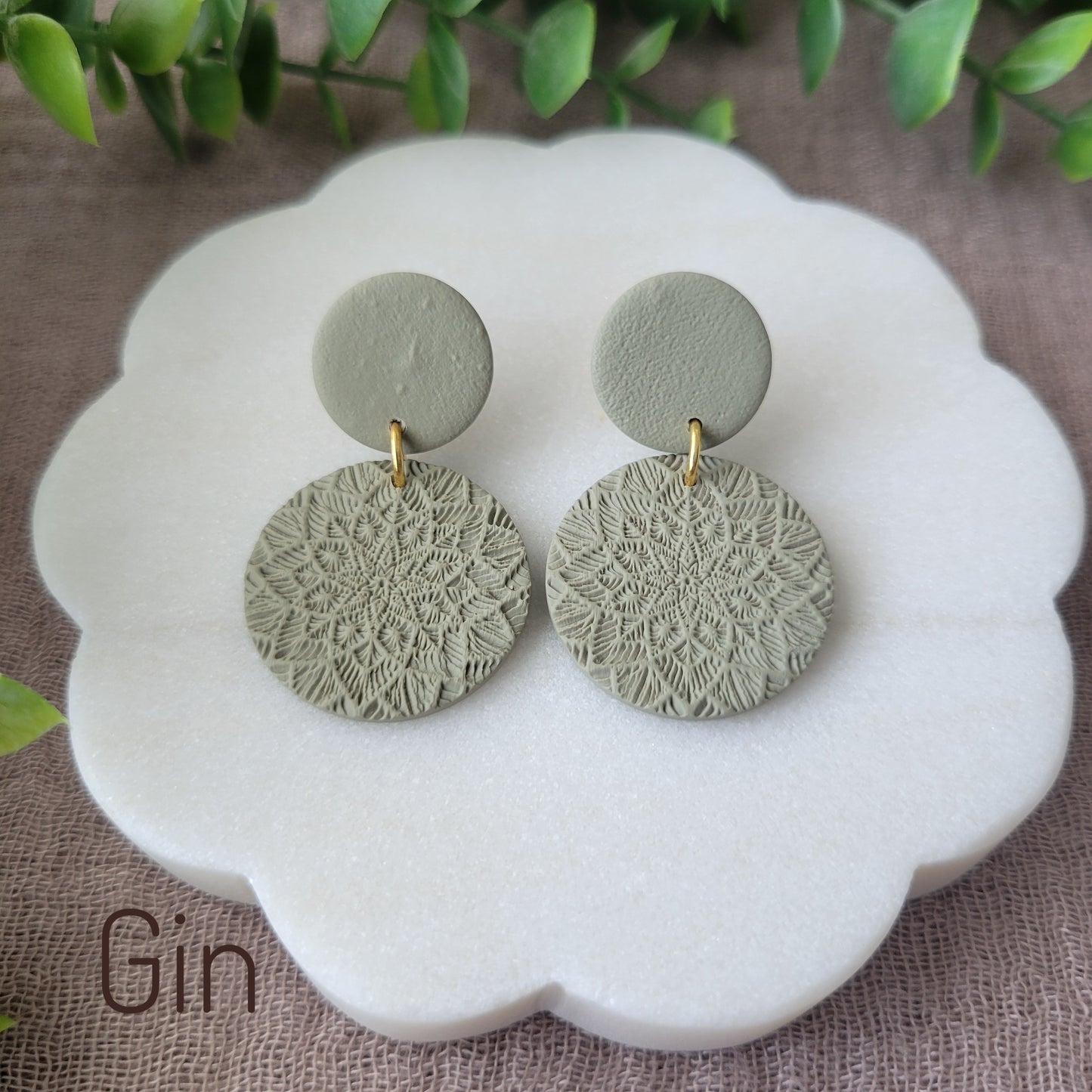 Top view of a pair of green mandala textured earrings displayed on a white round scalloped tray.