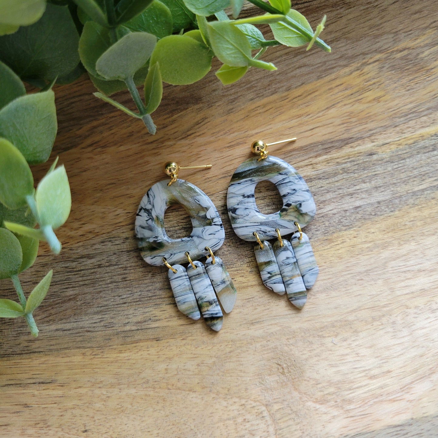 Top view of a pair of green, white, black, brown marbled earrings displayed on a wooden tray.