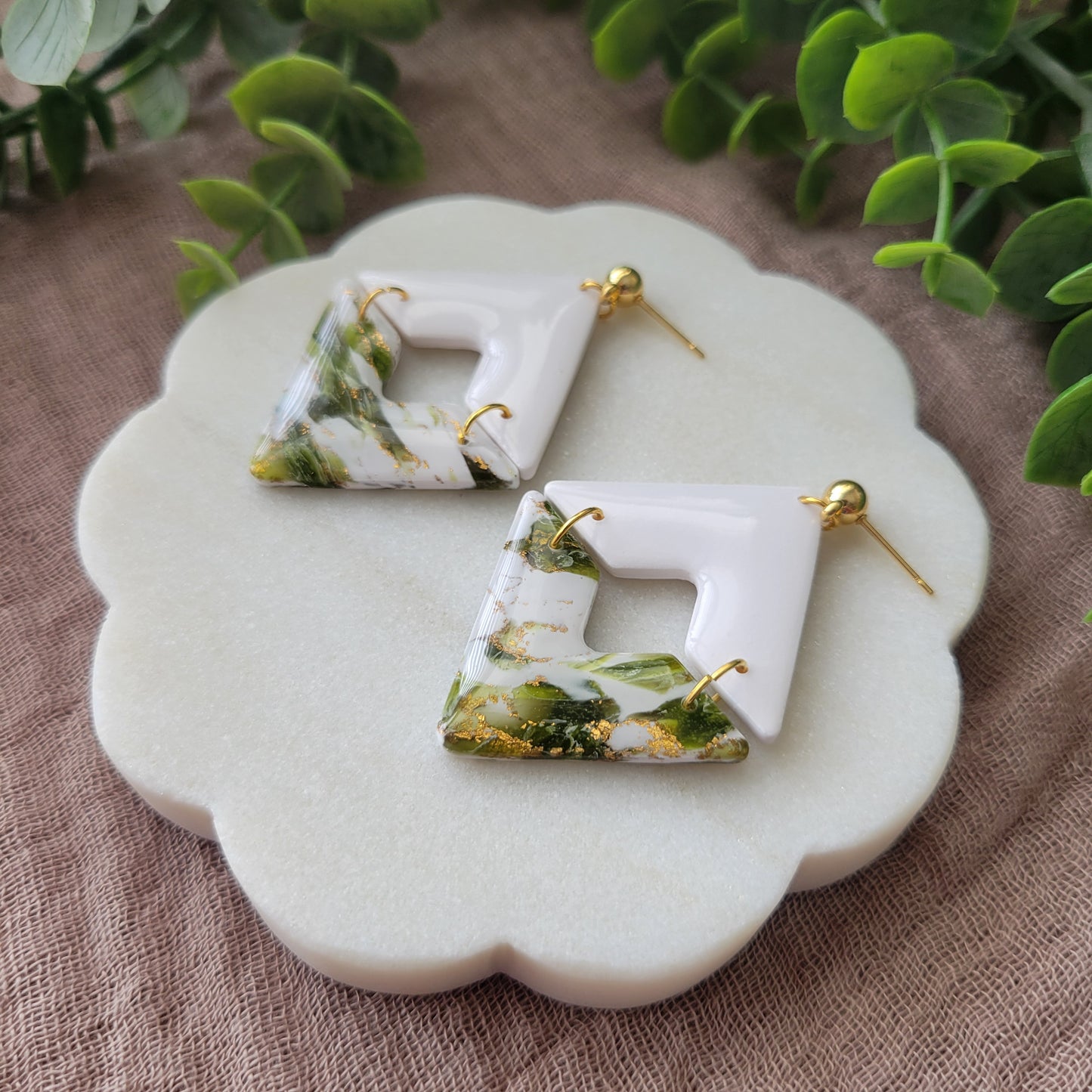 Right side view of a pair of white, green, gold accented geometric diamond earrings displayed on a white round scalloped tray.