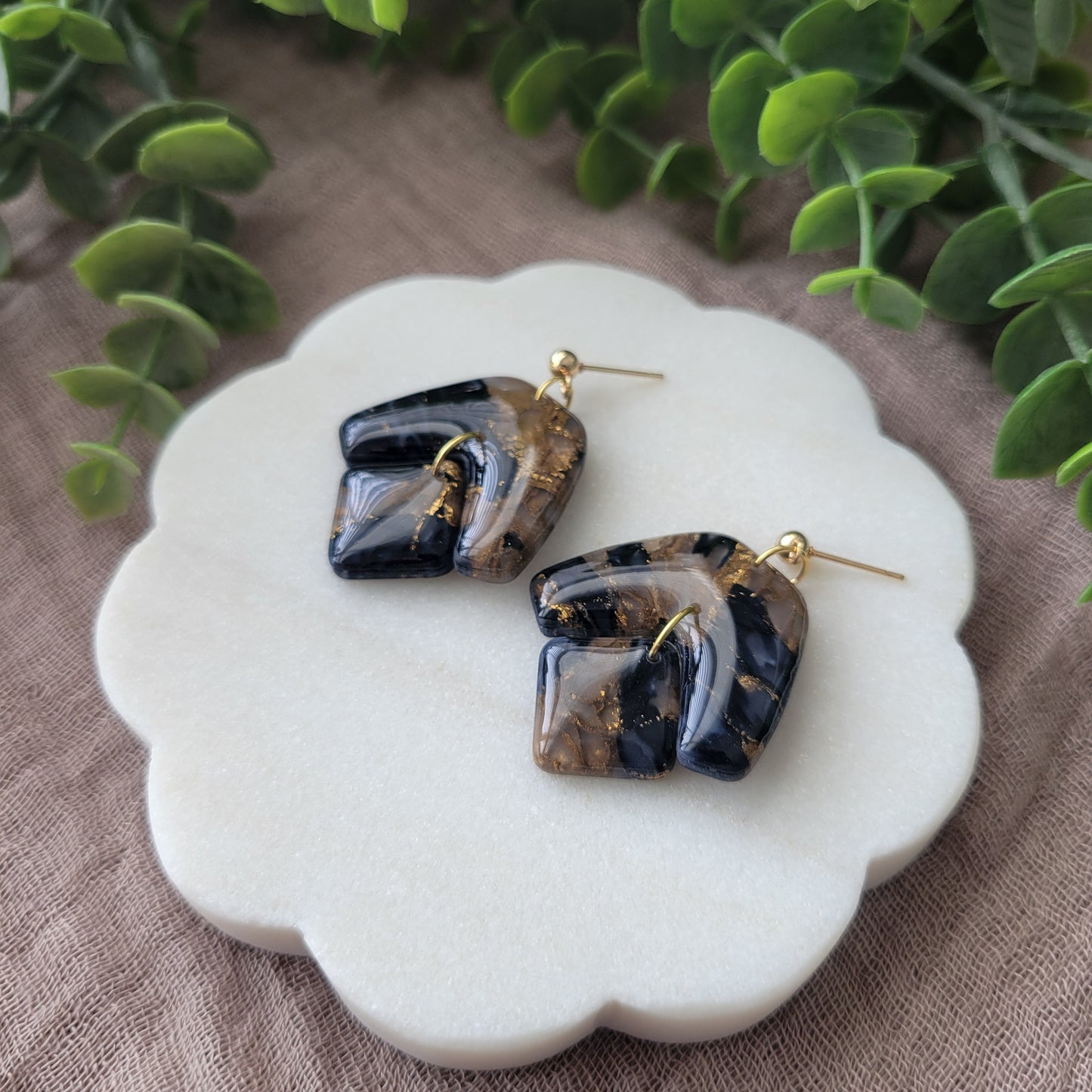 Right side view of a pair of dark blue, bronze marble boomerang shaped earrings displayed on a white round scalloped tray.
