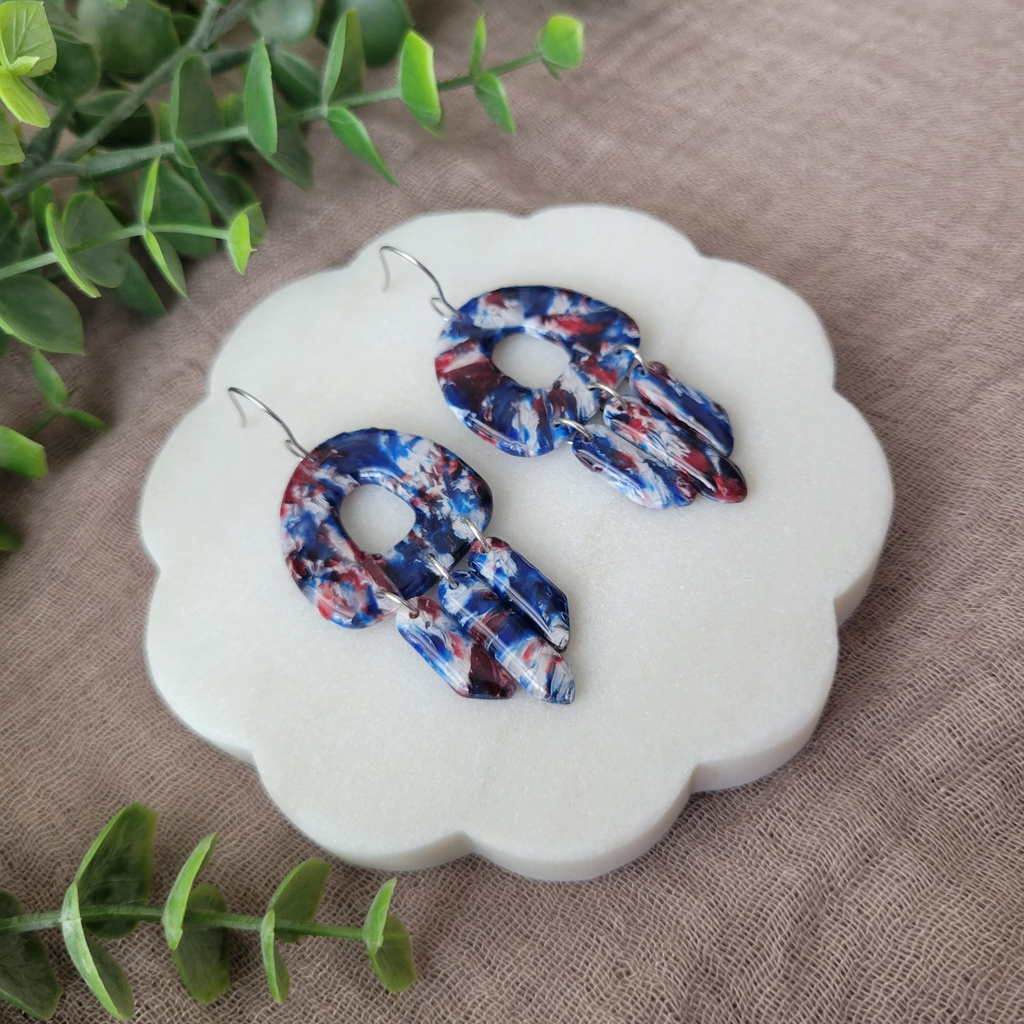 Left side view of a pair of red, white, blue marble earrings displayed on a white round scalloped tray.