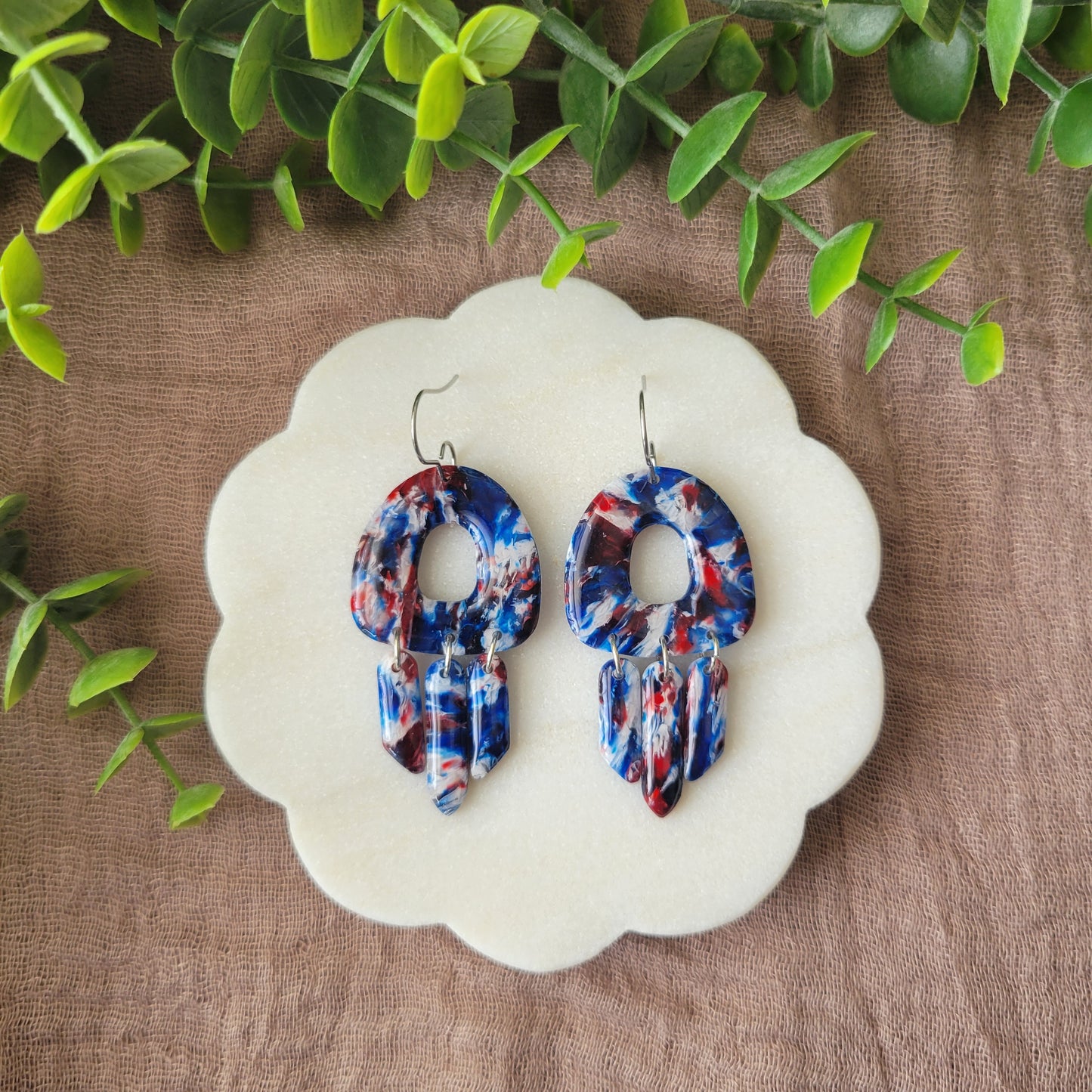Top view of a pair of red, white, blue marble earrings displayed on a white round scalloped tray.
