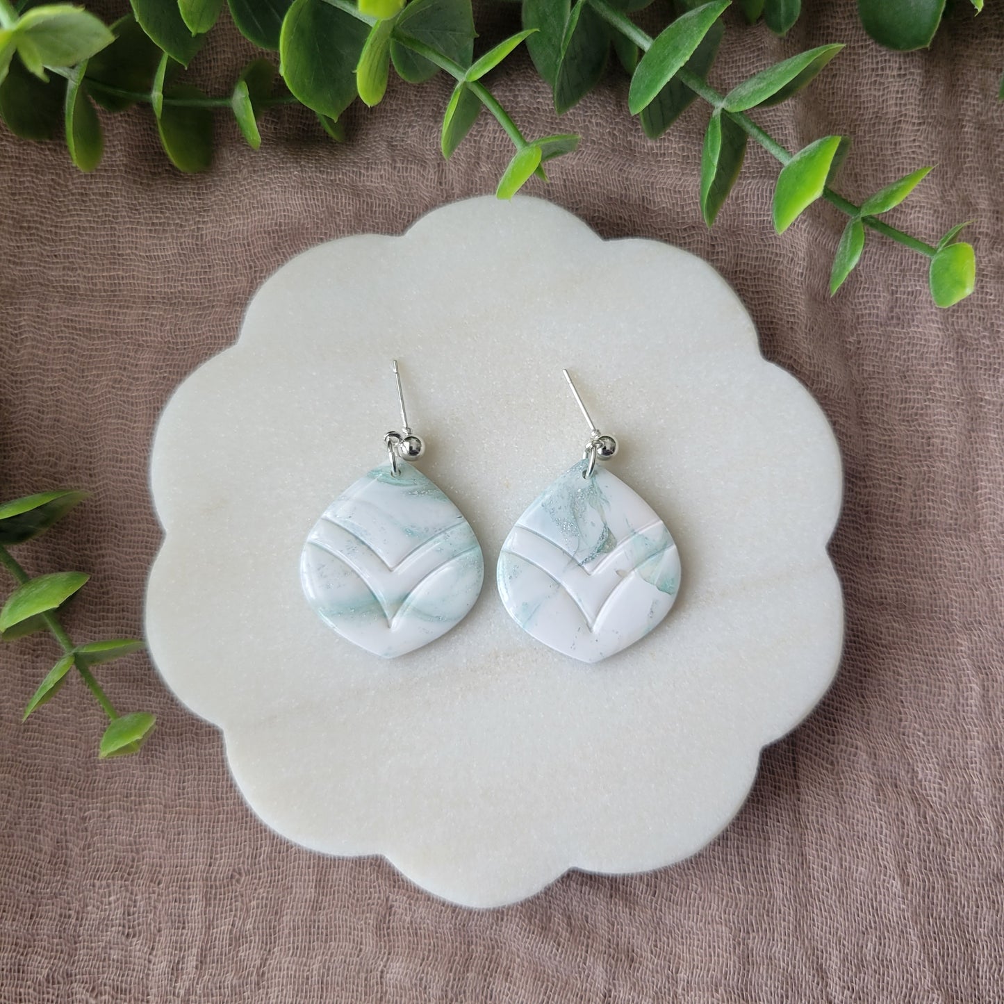 Top view of a pair of tiffany blue, white marble embossed round tear drop shaped earrings displayed on a white round scalloped tray.