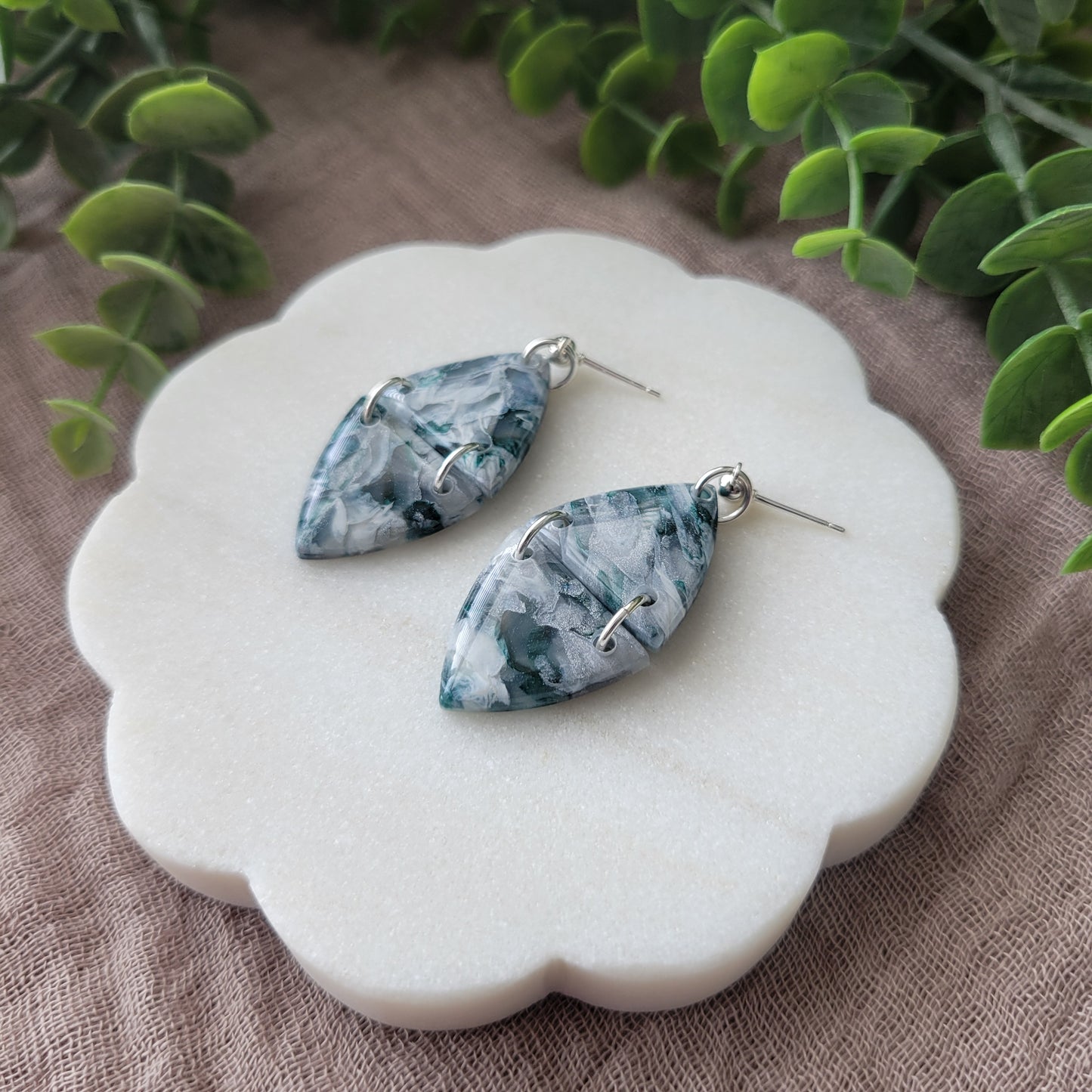 Right side view of a pair of green, white, silver marble earrings displayed on a white round scalloped tray.