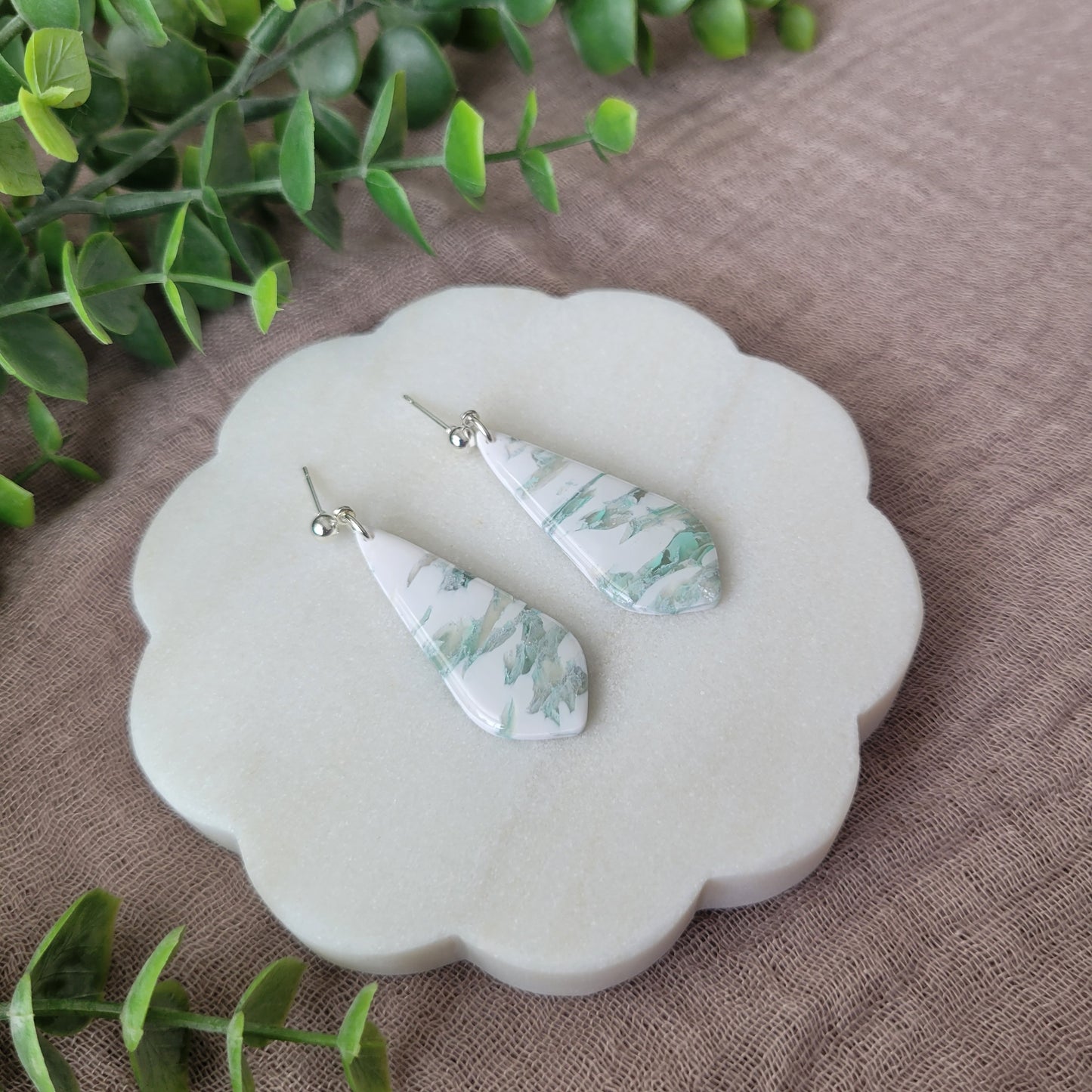 Left side view of a pair of tiffany blue, white marble elongated tear drop shaped earrings displayed on a white scalloped tray.