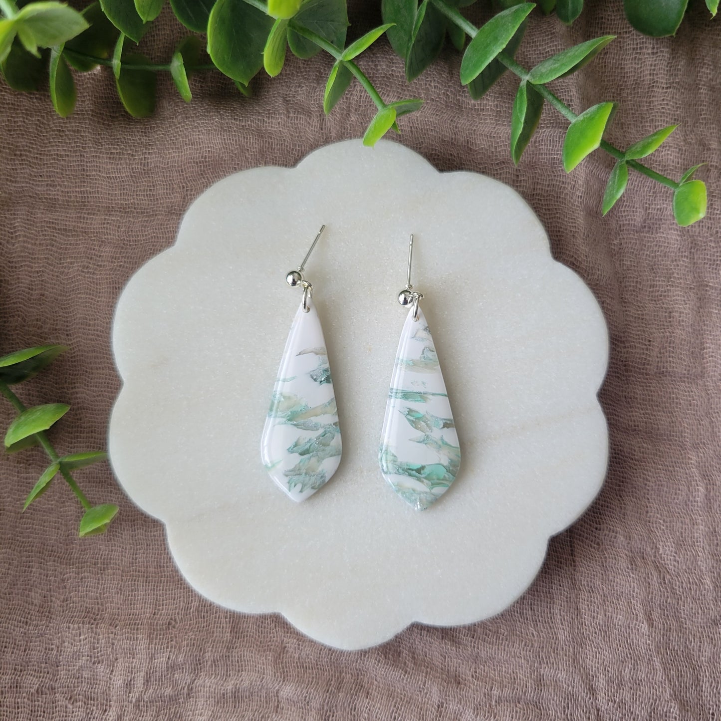 Top view of a pair of tiffany blue, white marble elongated tear drop shaped earrings displayed on a white scalloped tray.