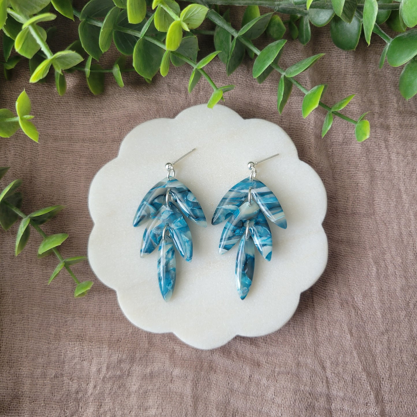 Top view of a pair of blue marble long leaf shaped earrings displayed on a white round scalloped tray.