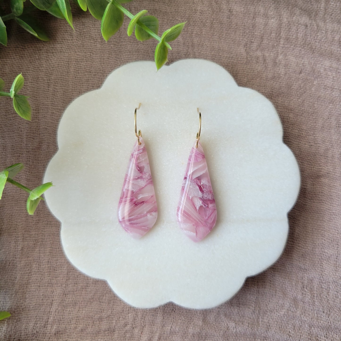 Top view of a pair of pink marble long teardrop shaped earrings displayed on a white round scalloped tray.