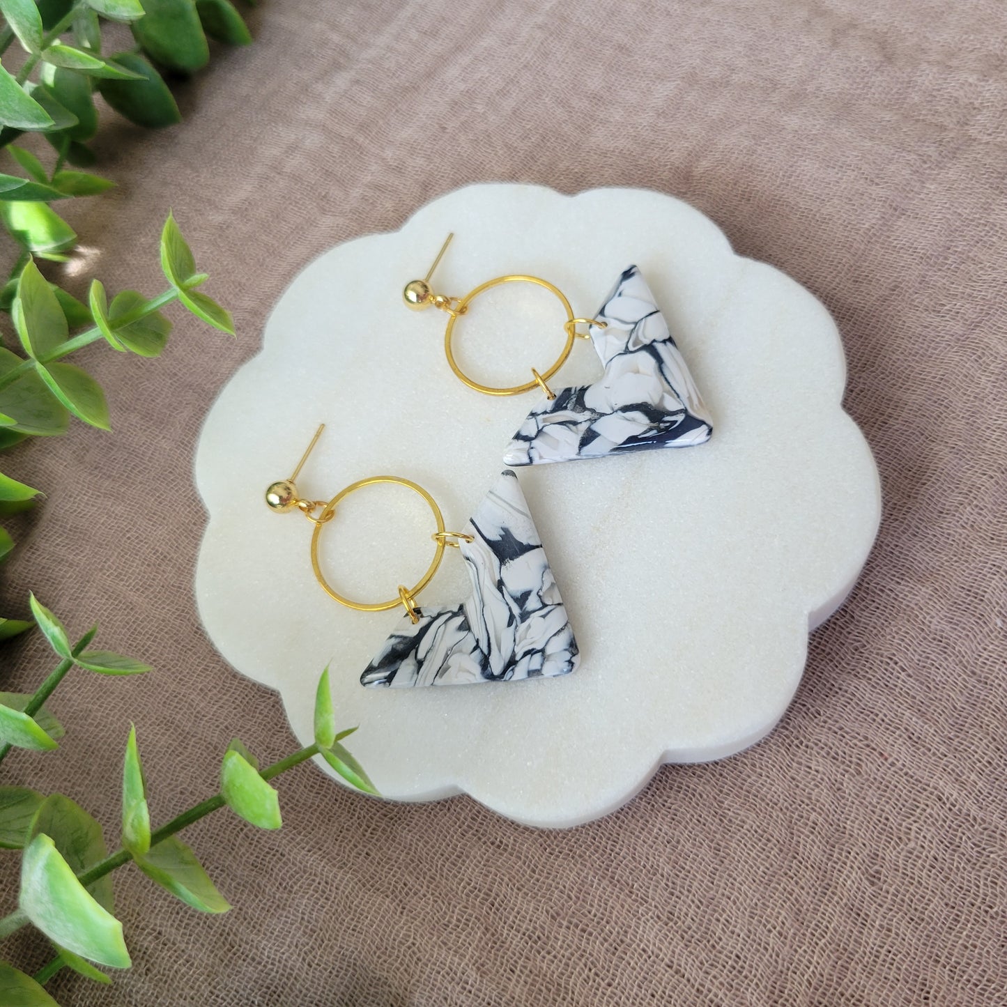 Left side view of a pair of black, white marbled chevron shaped earrings with a gold circle bezel displayed on a white round scalloped tray.