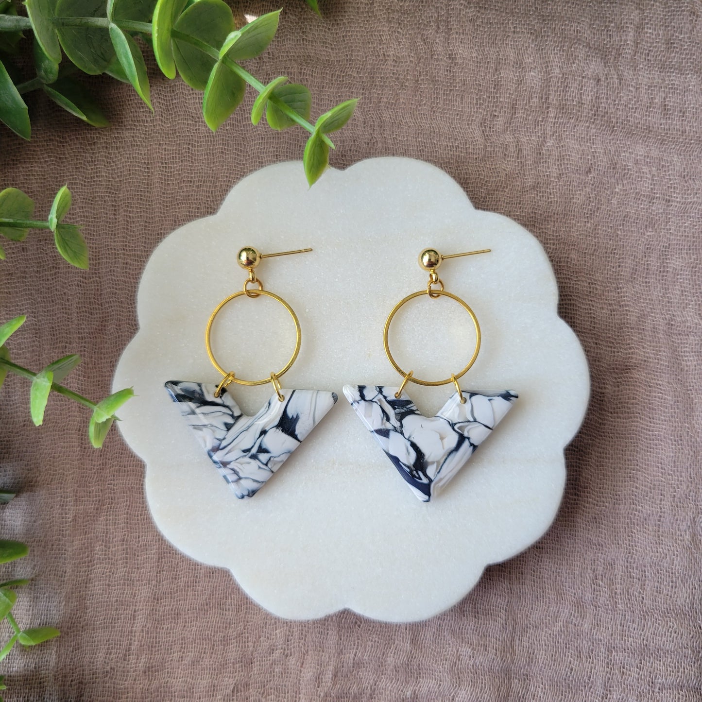 Top view of a pair of black, white marbled chevron shaped earrings with a gold circle bezel displayed on a white round scalloped tray.