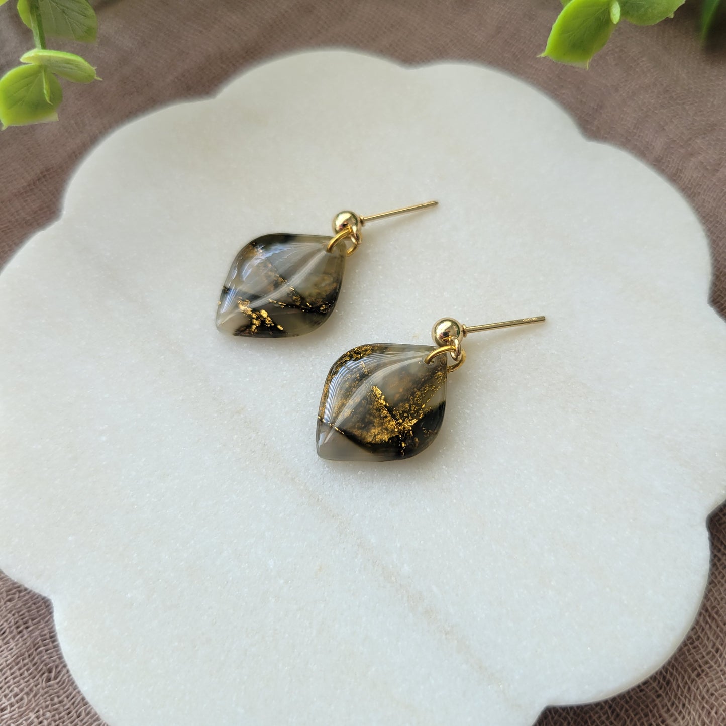 Right side view of a pair of moss green marble diamond shaped earrings displayed on a white round scalloped tray.