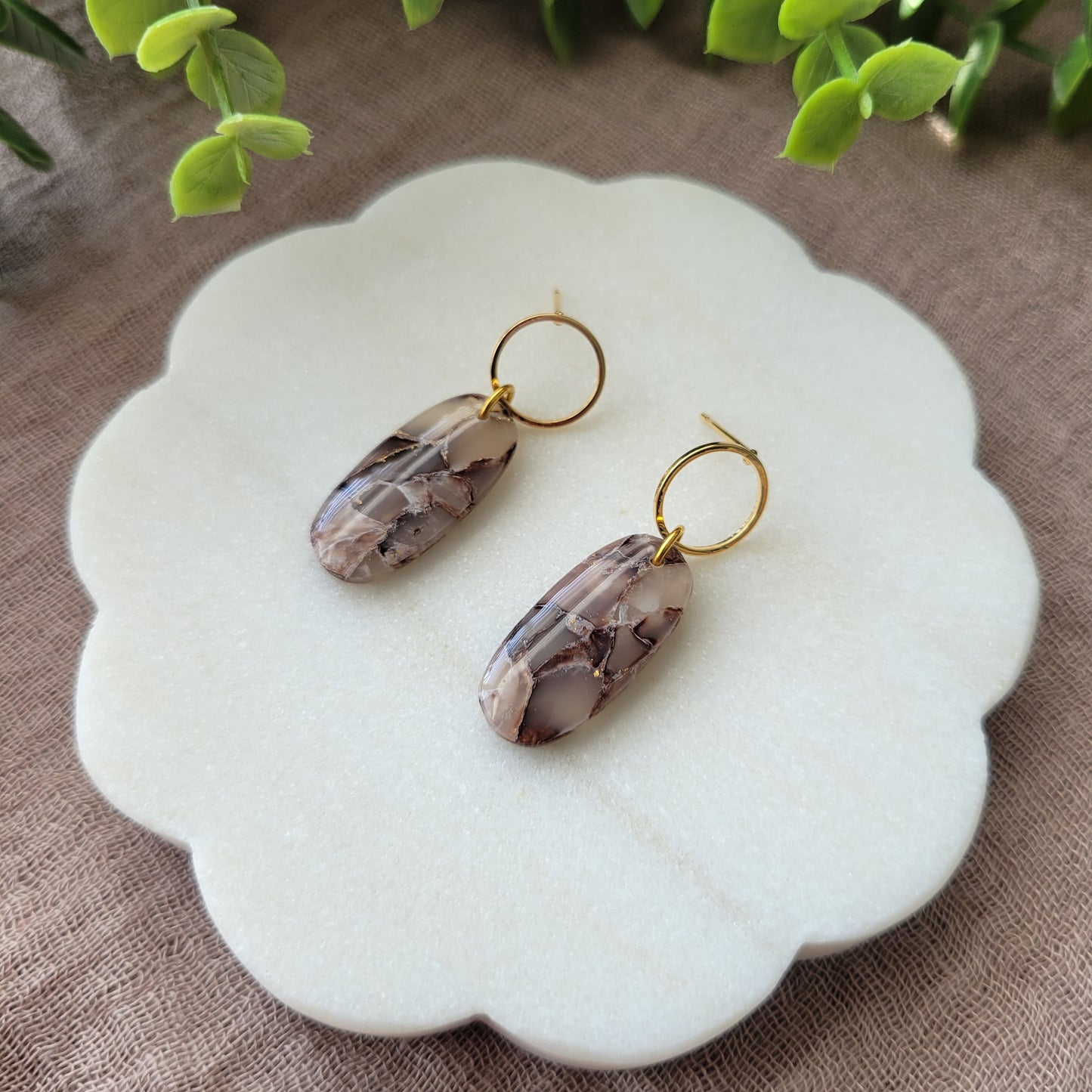 Right side view of a pair of brown marble long oval earrings displayed on a white round scalloped tray.