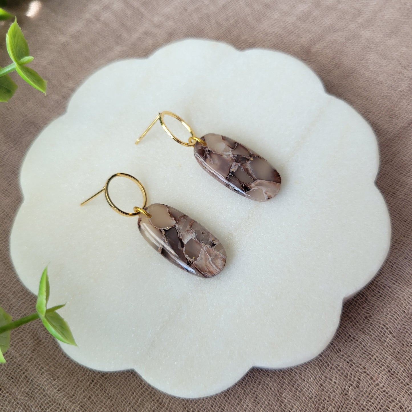 Left side view of a pair of brown marble long oval earrings displayed on a white round scalloped tray.