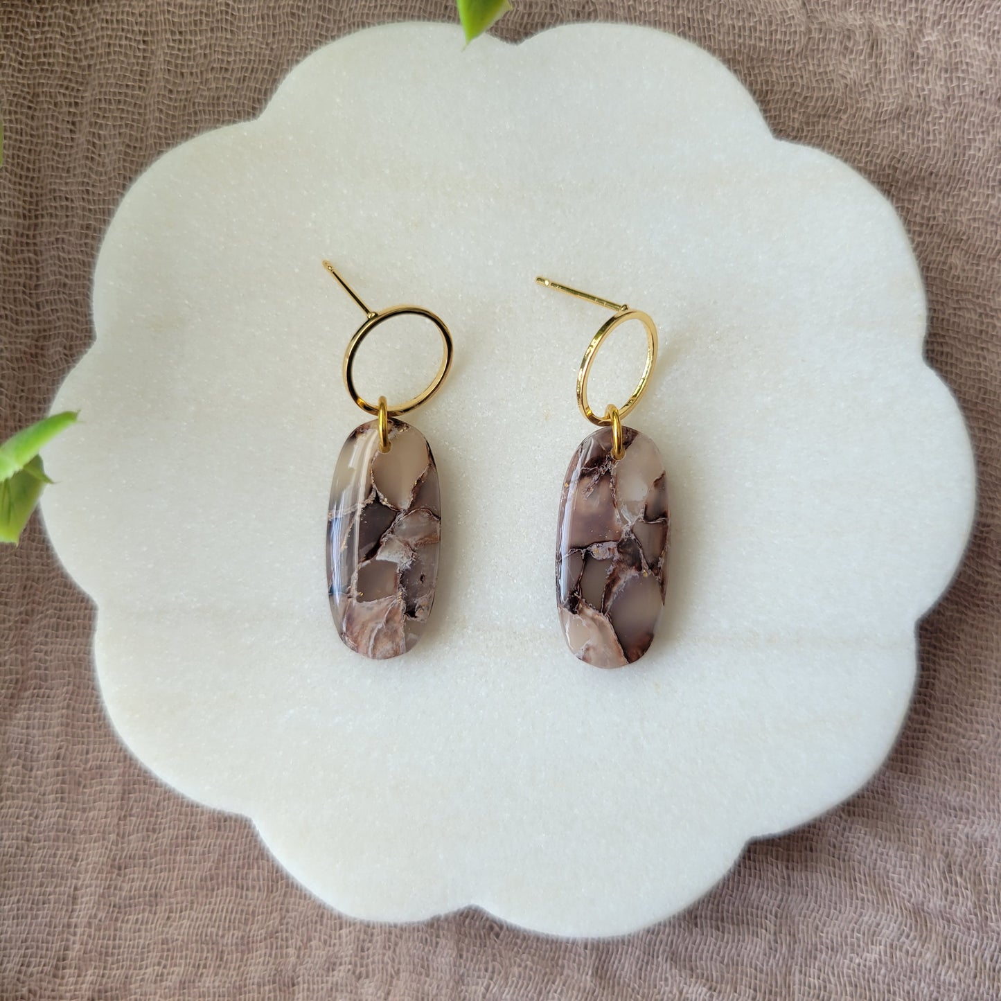 Top view of a pair of brown marble long oval earrings displayed on a white round scalloped tray.