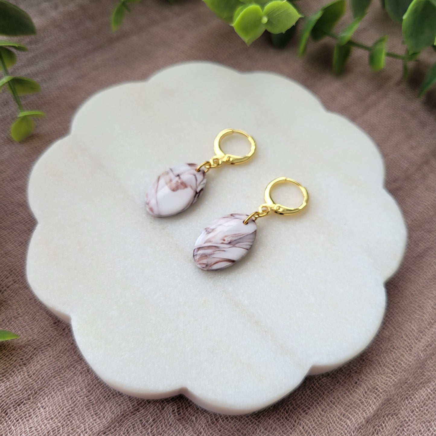 Right side view of a pair of brown, white marble oval shaped earrings displayed on a white round scalloped tray.