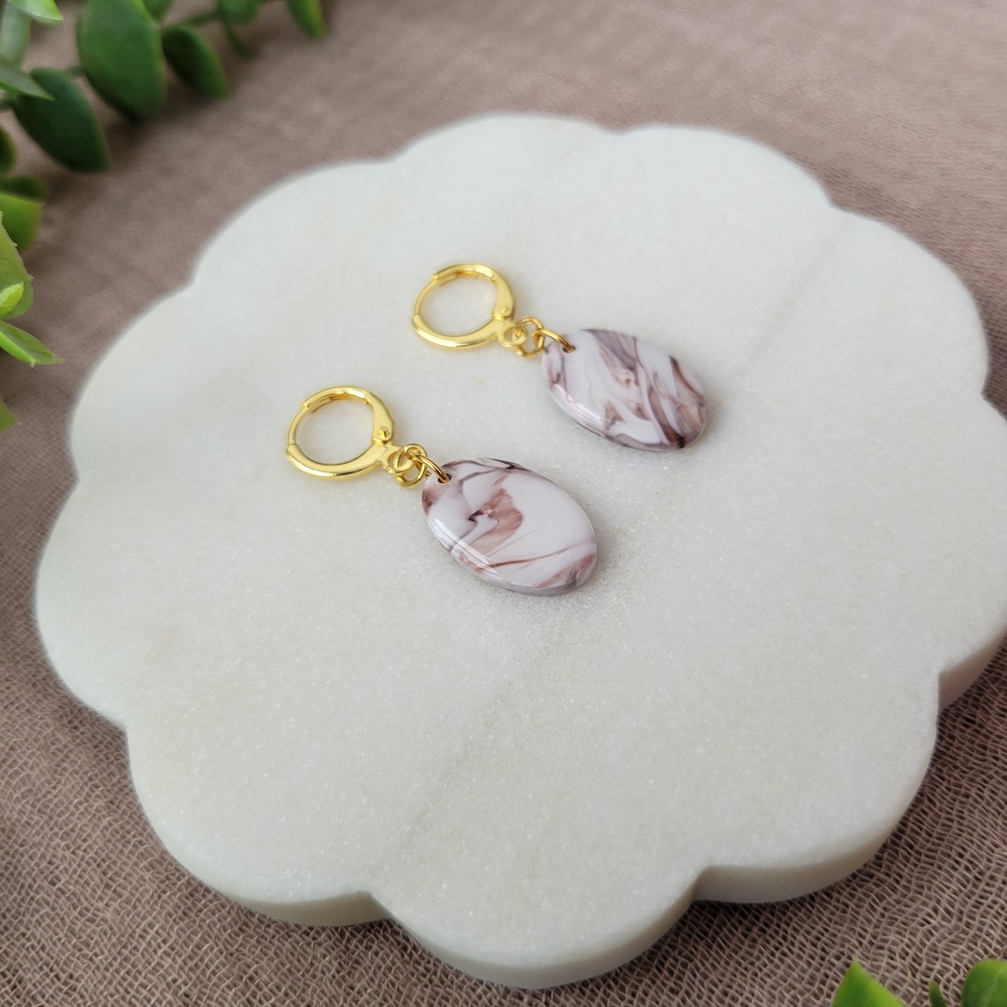 Left side view of a pair of brown, white marble oval shaped earrings displayed on a white round scalloped tray.