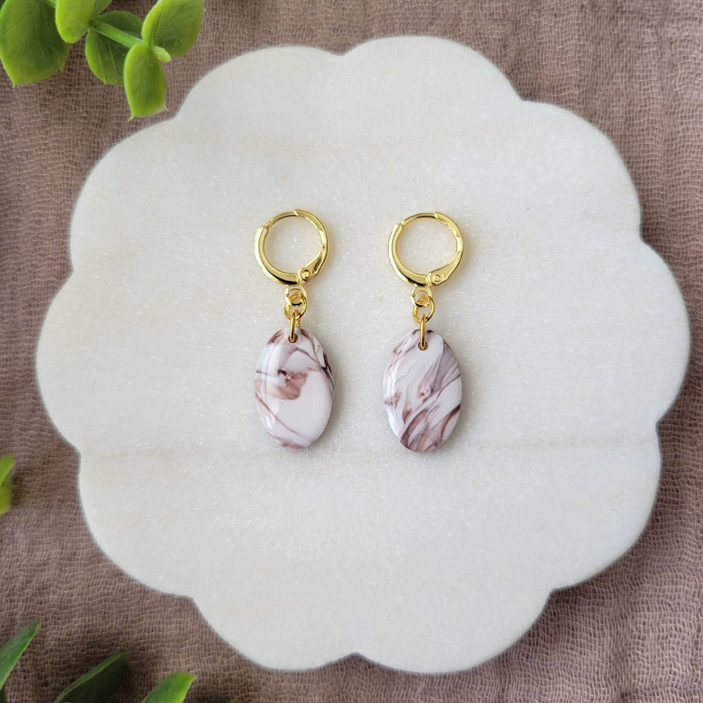 Top view of a pair of brown, white marble oval shaped earrings displayed on a white round scalloped tray.