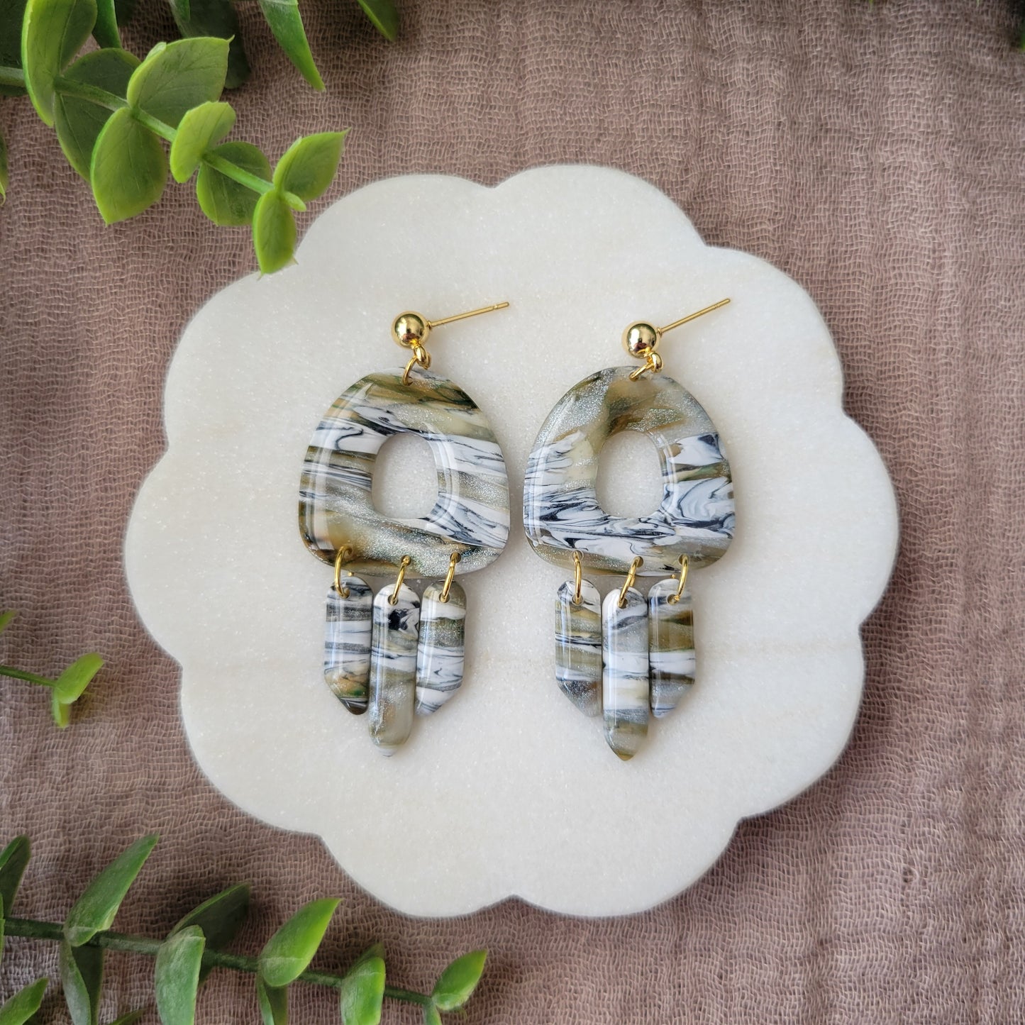 Top view of a pair of green, white, black, brown marbled earrings displayed on a white round scalloped tray.