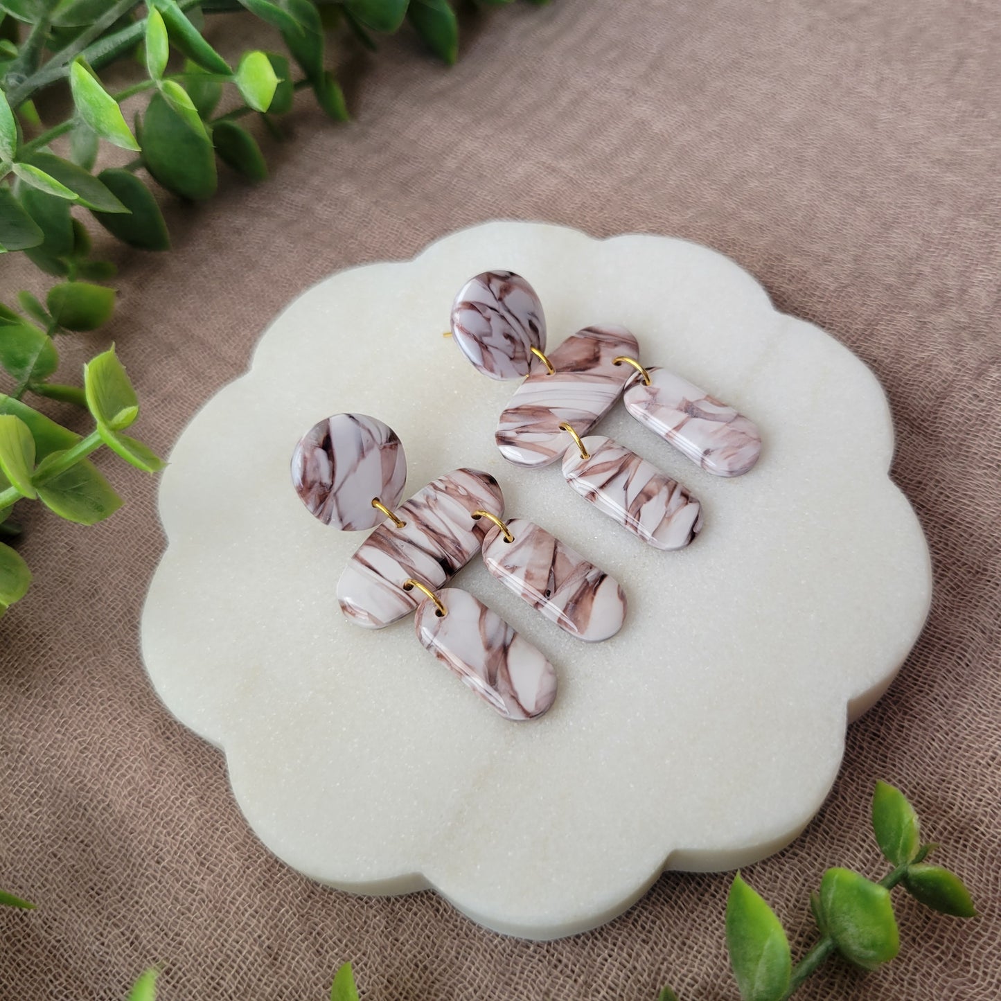 Left side view of a pair of brown, white marble stone shaped earrings displayed on a white round scalloped tray.