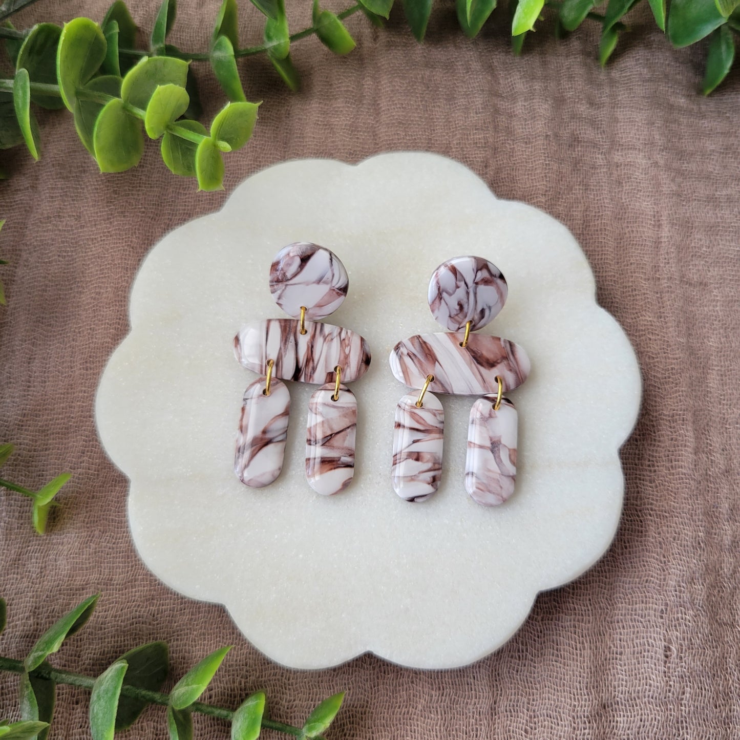 Top view of a pair of brown, white marble stone shaped earrings displayed on a white round scalloped tray.