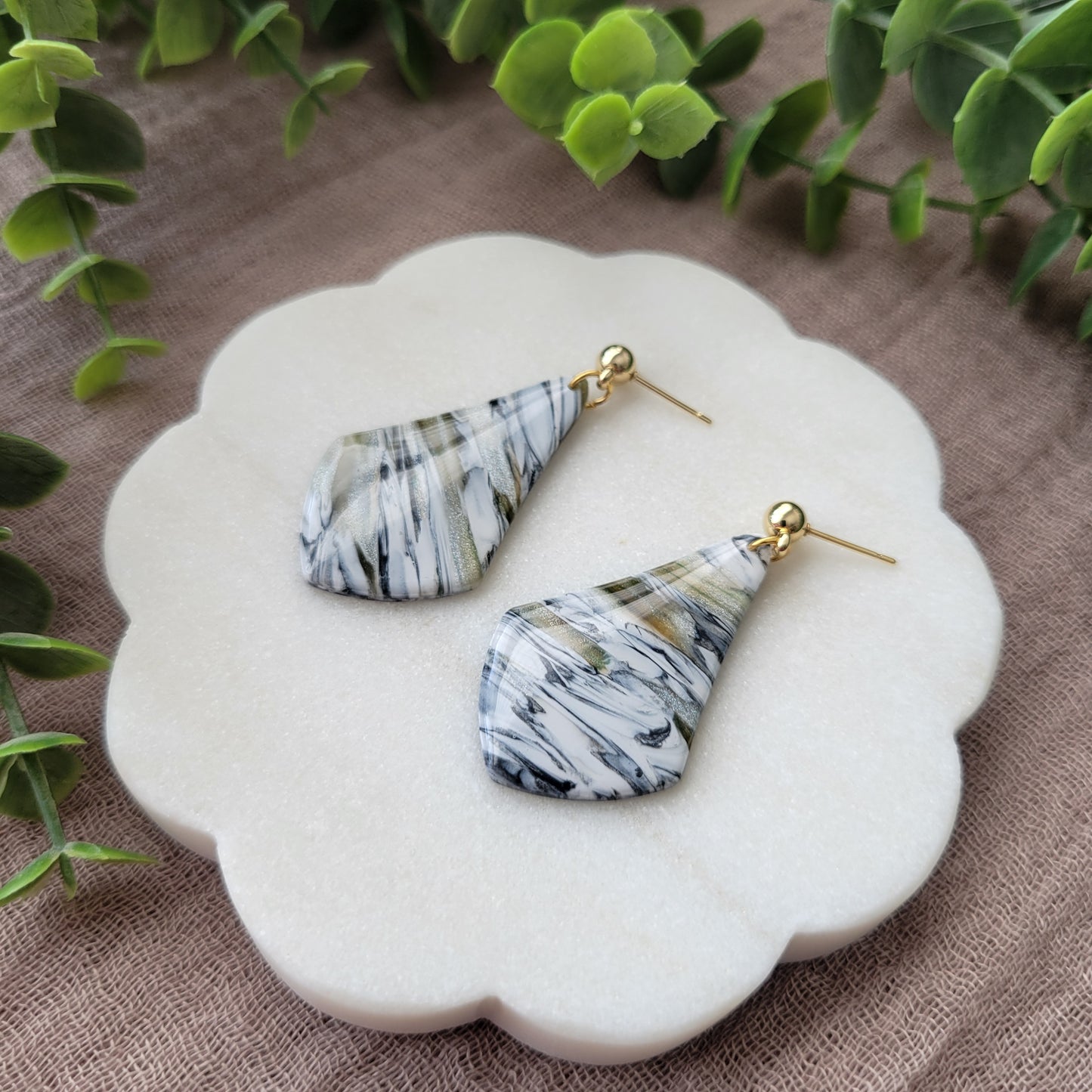 Right side view of a pair of black, white, brown, moss wide teardrop shaped earrings displayed on a white round scalloped tray.