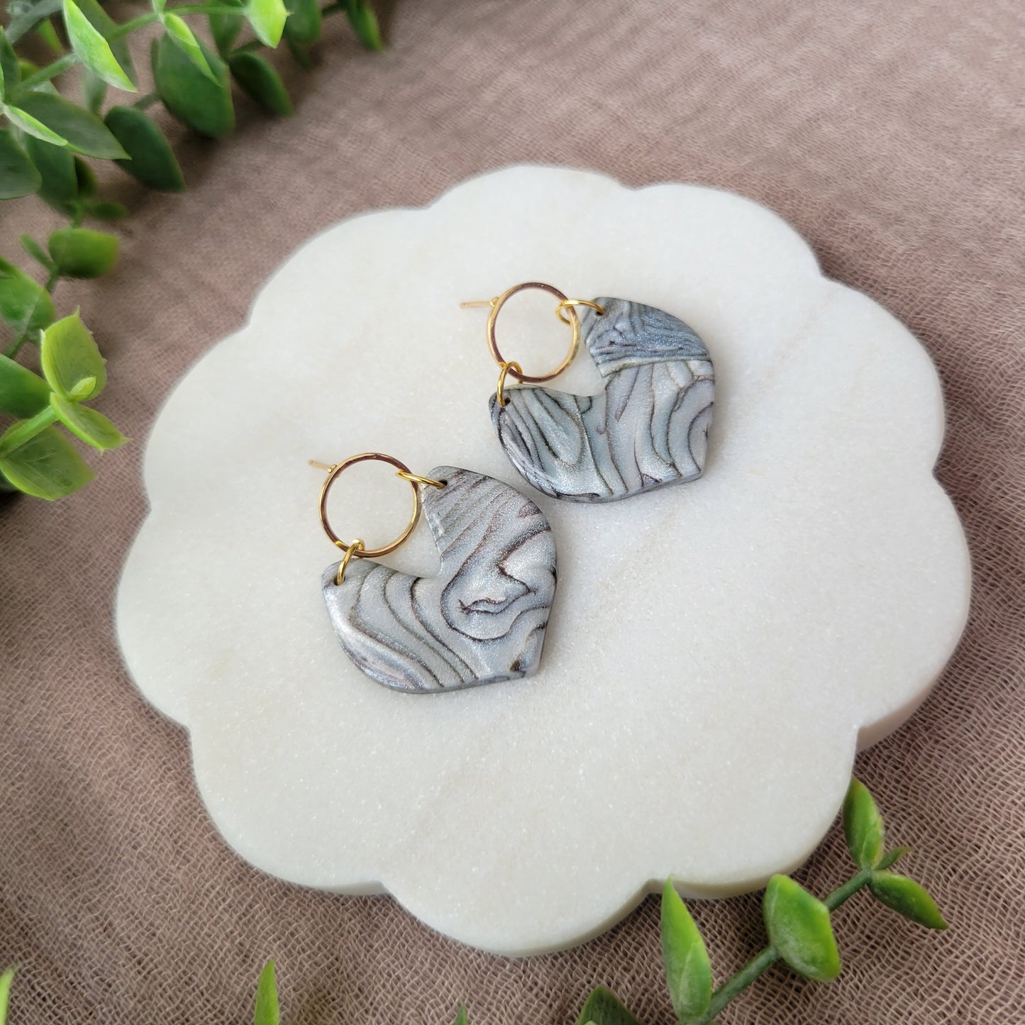 Left side view of a pair of silver, brown earrings displayed on a white round scalloped tray.