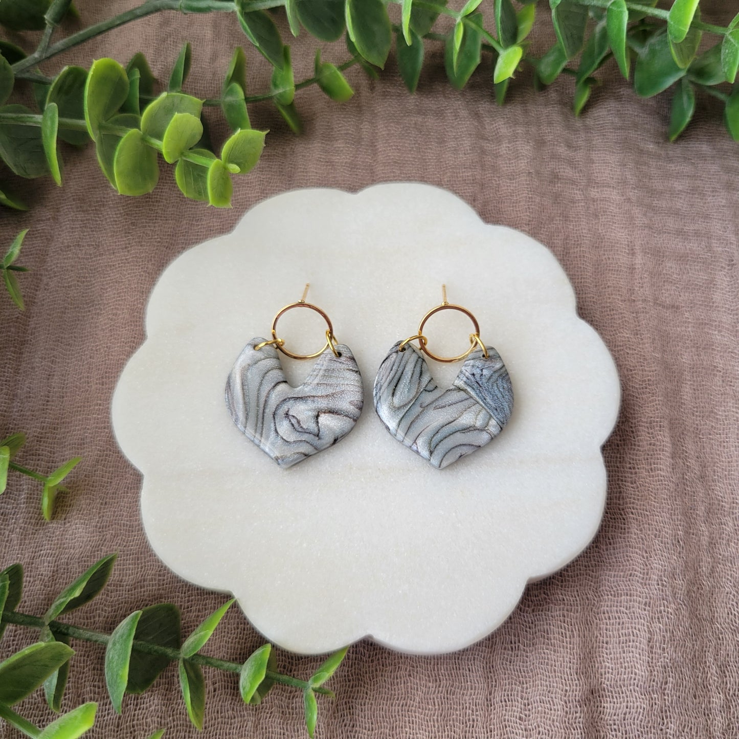 Top view of a pair of silver, brown earrings displayed on a white round scalloped tray.
