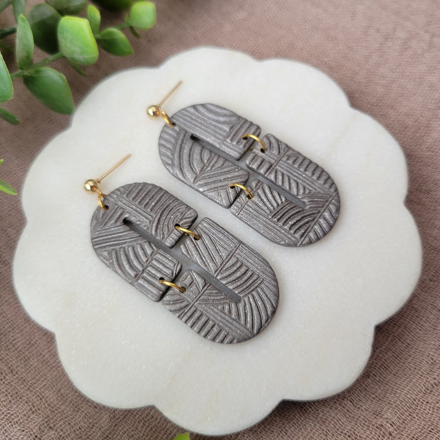 Left side view of a pair of gray earrings with art deco lines texture displayed on a white round scalloped tray.