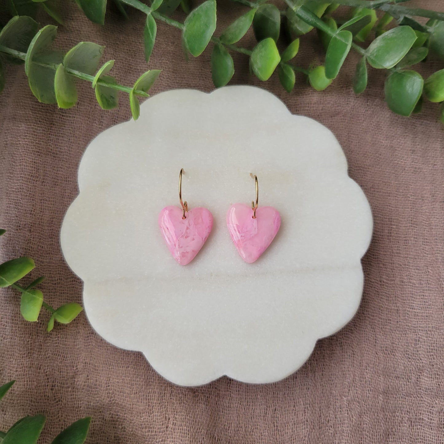 Top view of a pair of pink marble heart earrings displayed on a white round scalloped tray.