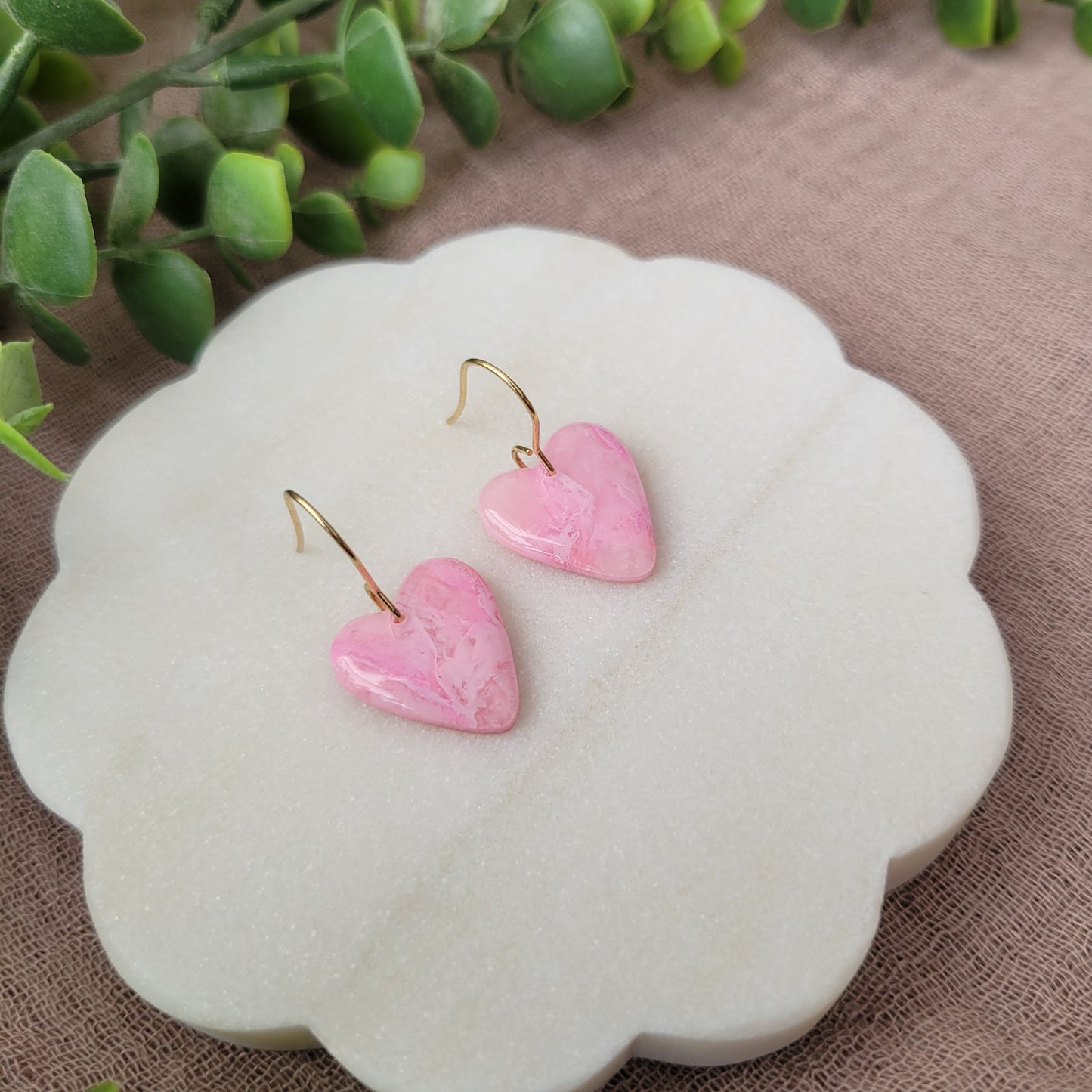 Left side view of a pair of pink marble heart earrings displayed on a white round scalloped tray.