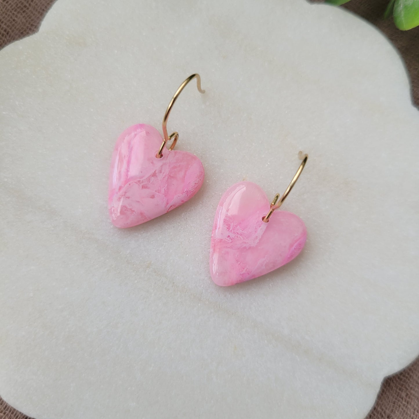 Close up top view of a pair of pink marble heart earrings displayed on a white round scalloped tray.