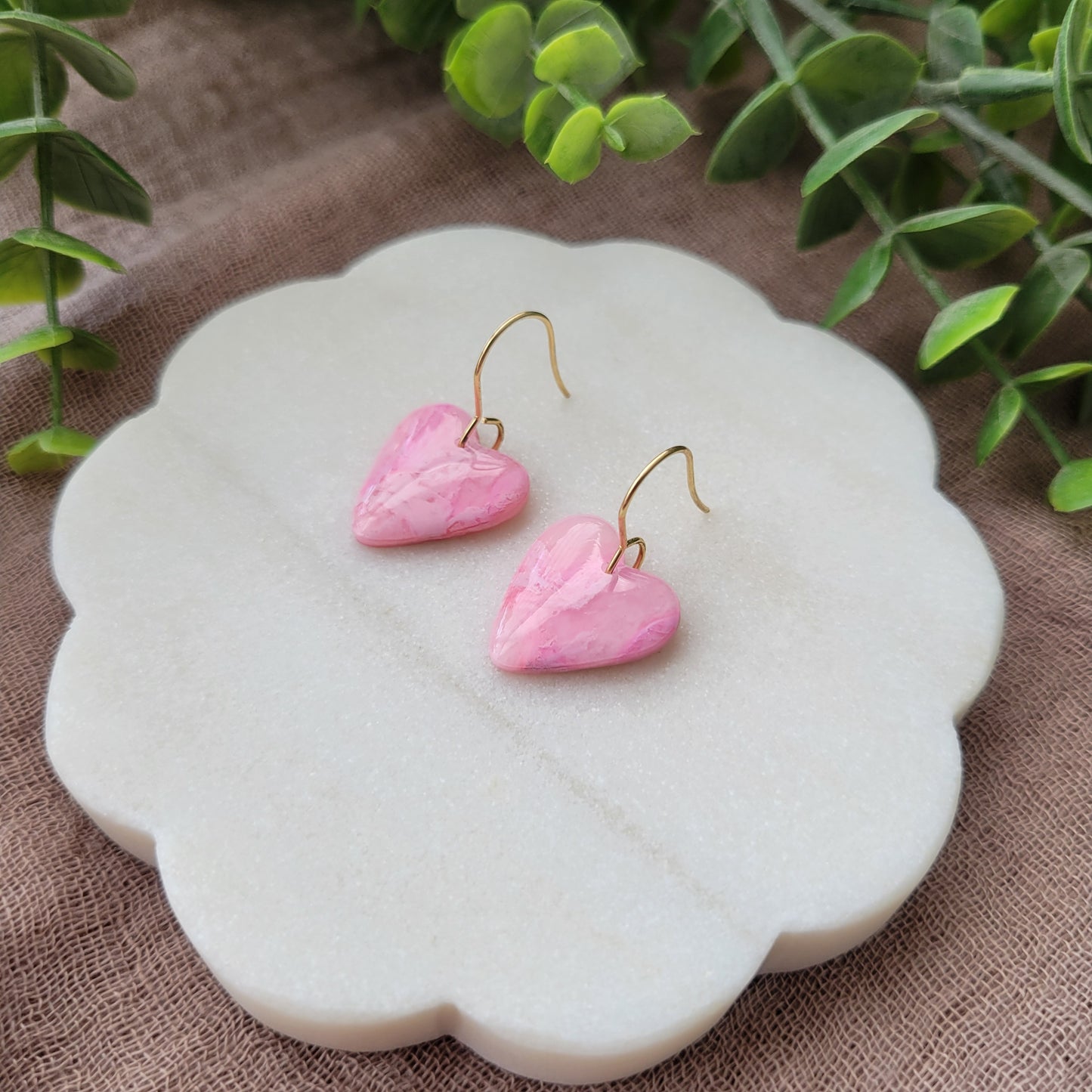 Right side view of a pair of pink marble heart earrings displayed on a white round scalloped tray.