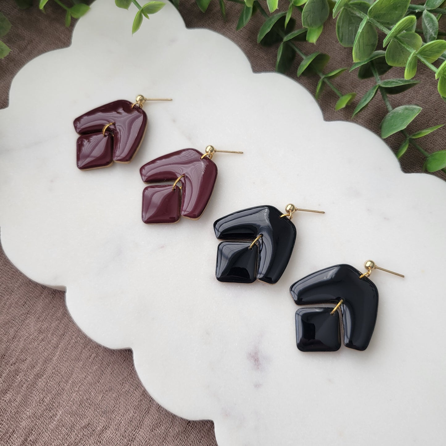 Side view of two pairs of earrings with shiny resin displayed on a white scalloped tray.